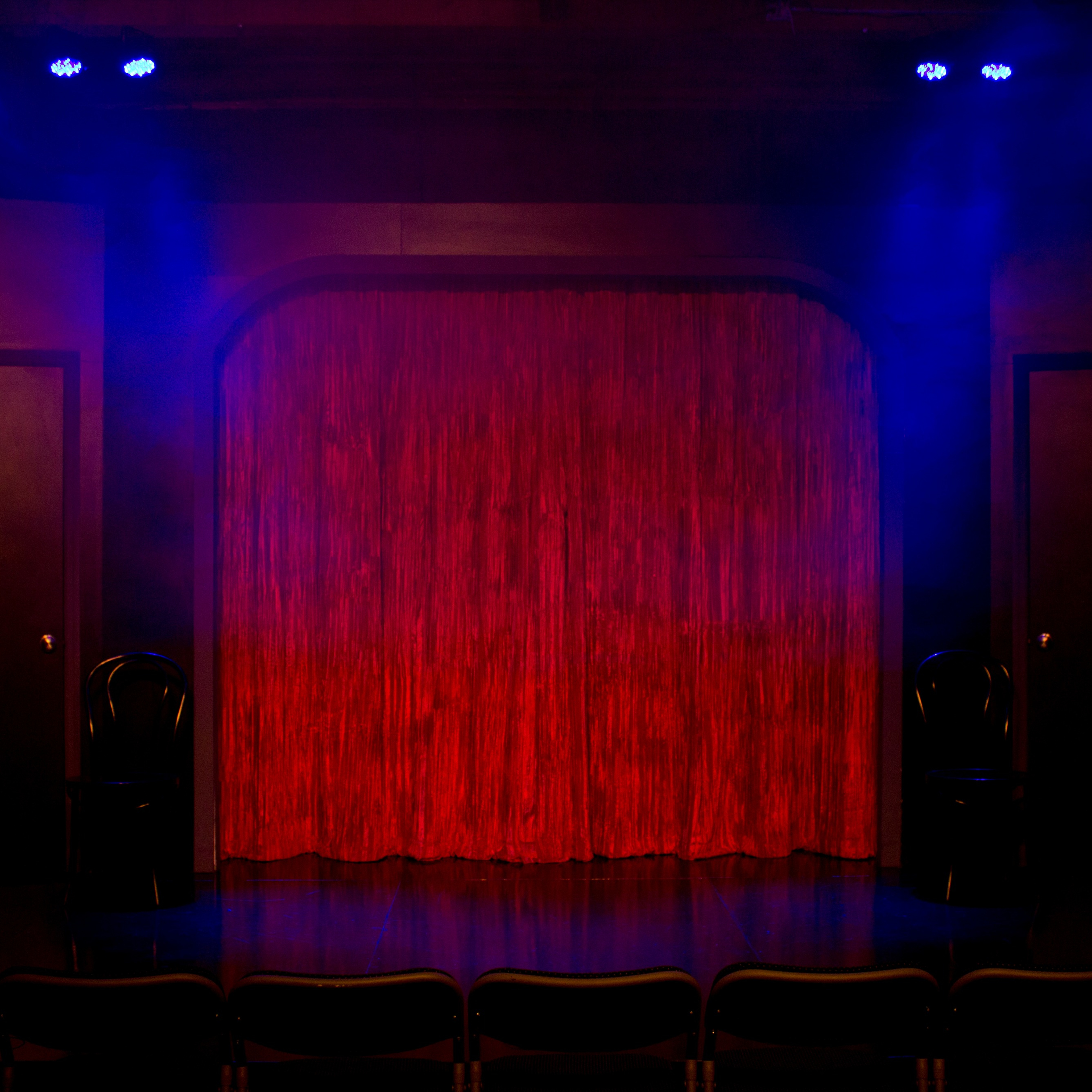 A dimly lit stage with a red curtain and two chairs positioned on either side, ready for a performance.