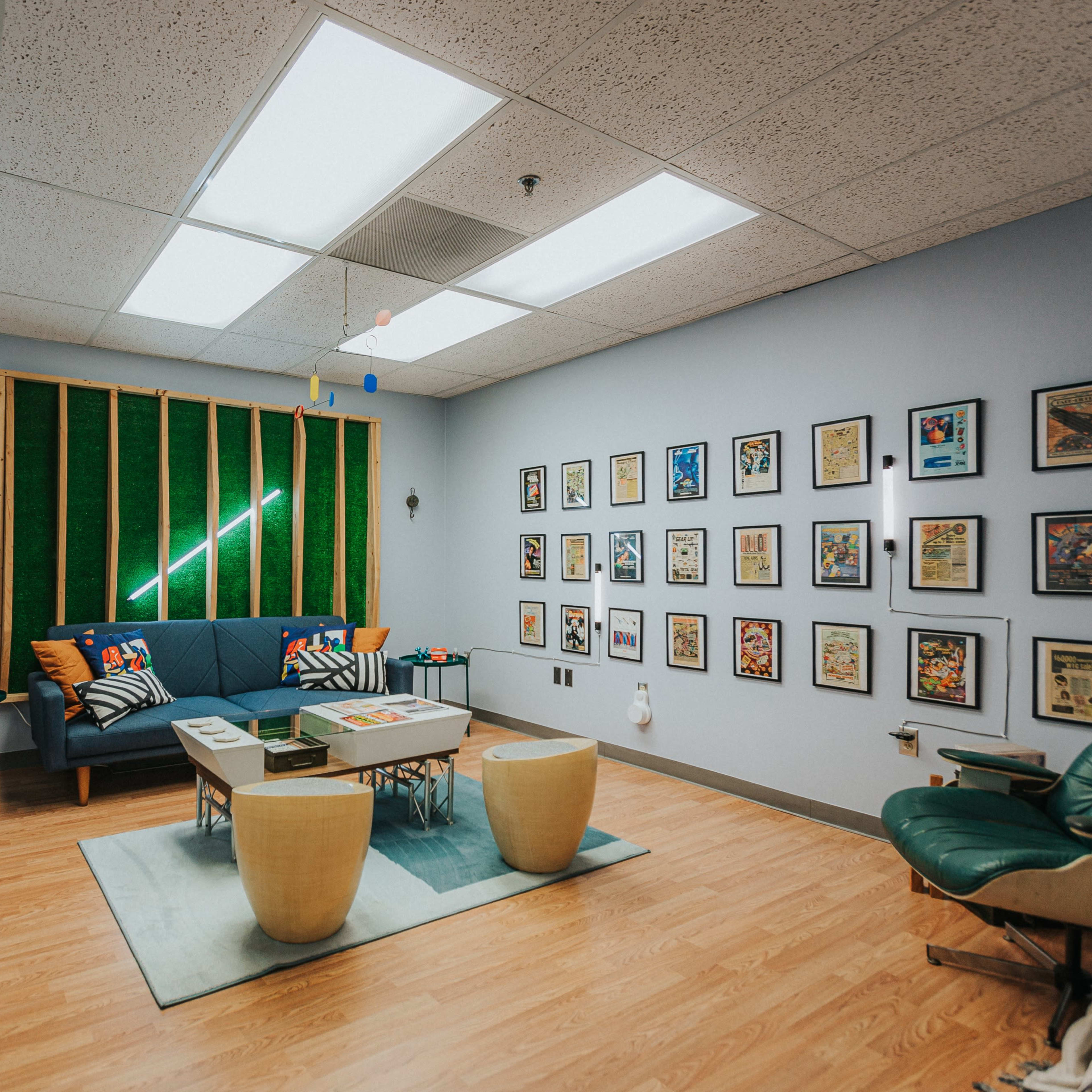 A modern room features a seating area with a couch and coffee table, surrounded by framed artwork on the walls and a green backdrop with ceiling lights.