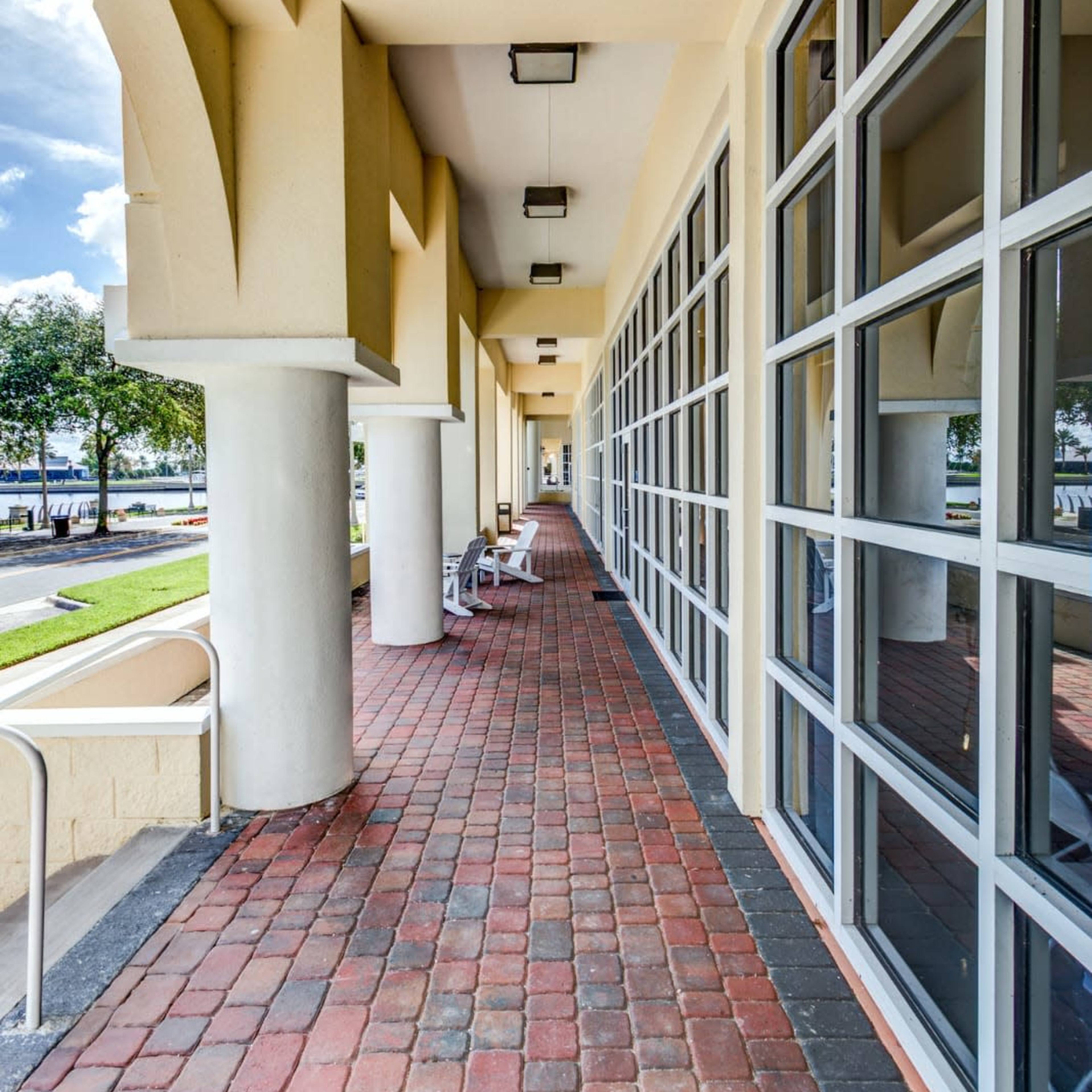 A brick-lined walkway bordered by large windows and columns, leading to an outdoor view.