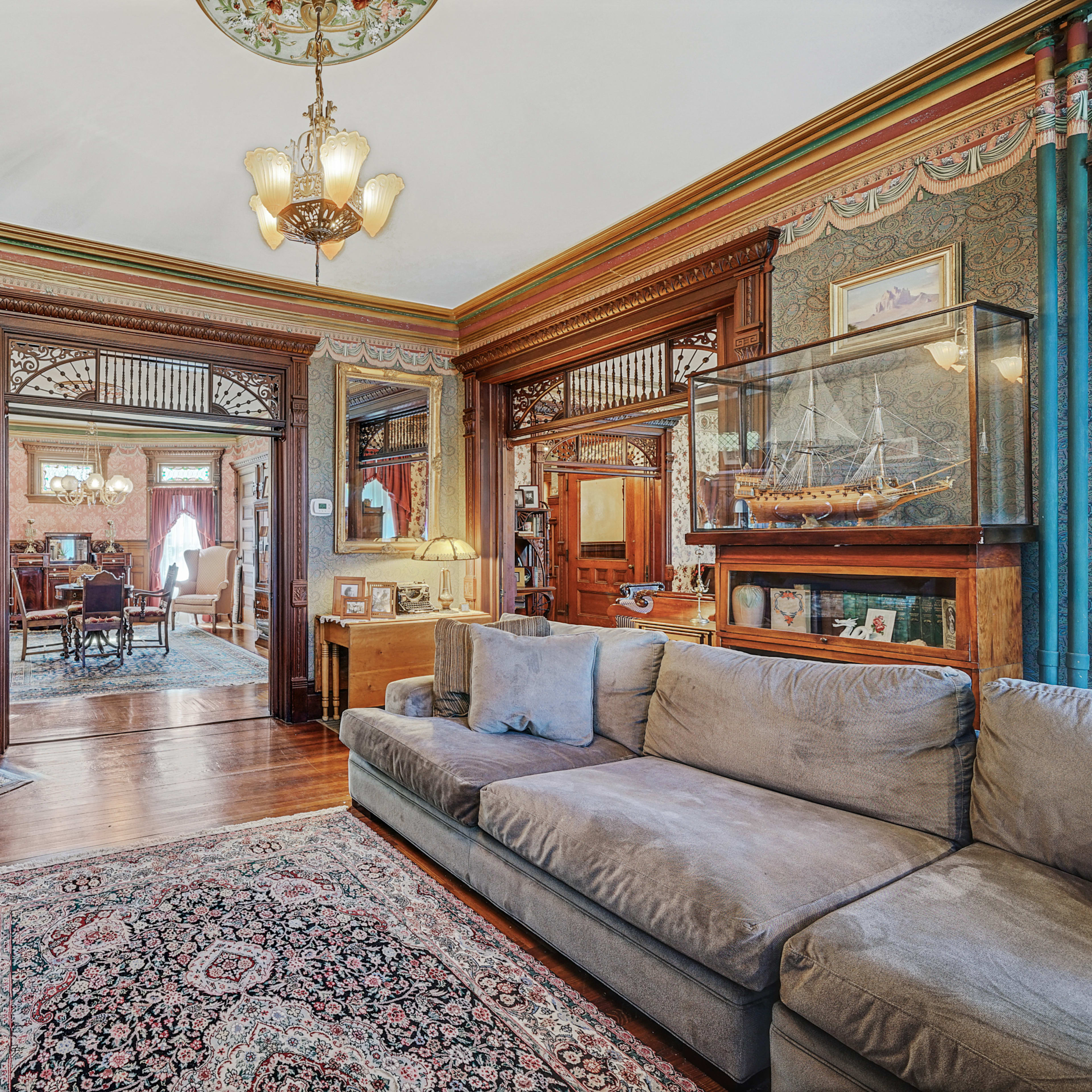 A vintage living room featuring ornate wooden paneling, two plush sofas, and a view of a dining area through an archway.