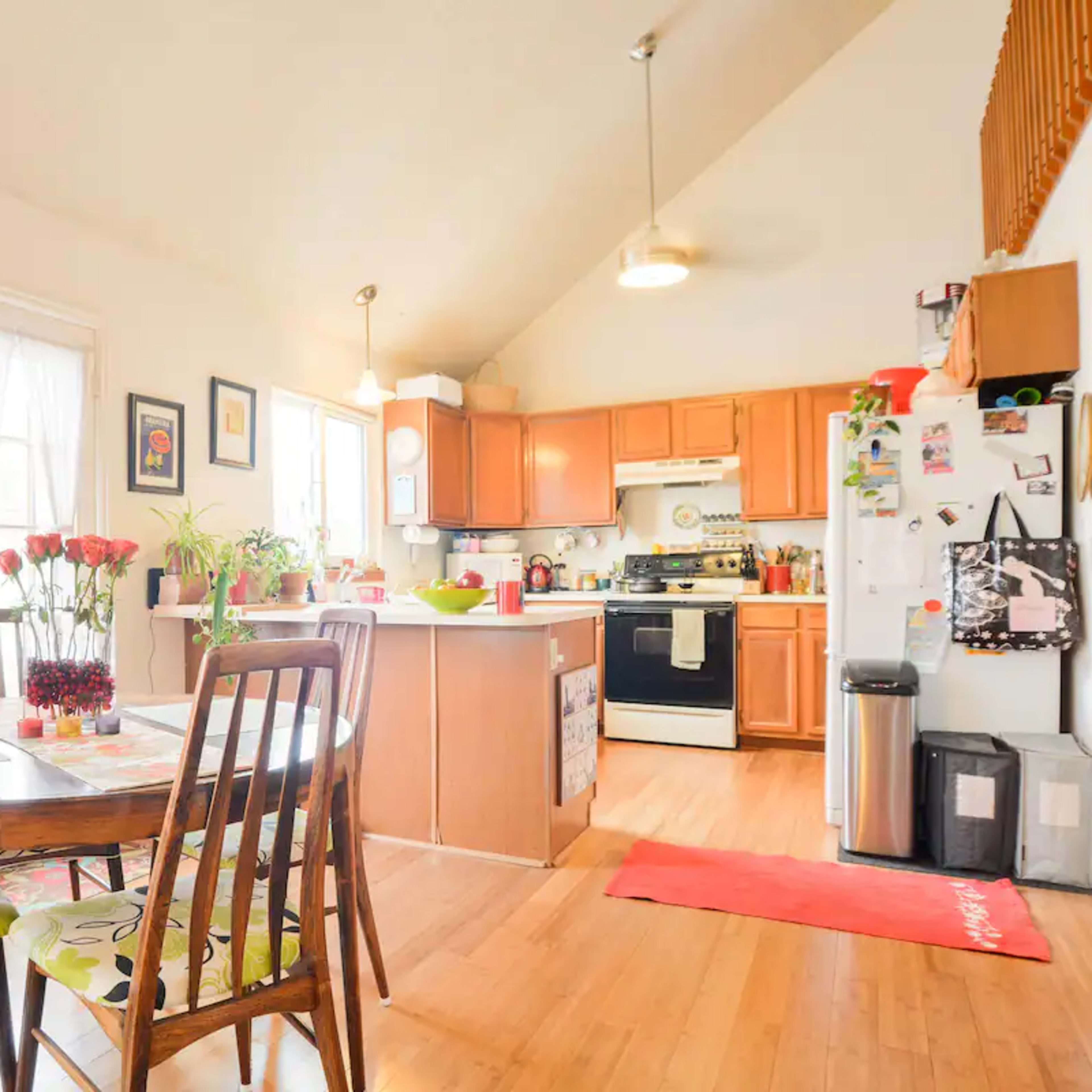 A bright kitchen features wooden cabinets, a dining table with four chairs, and a door leading outside.