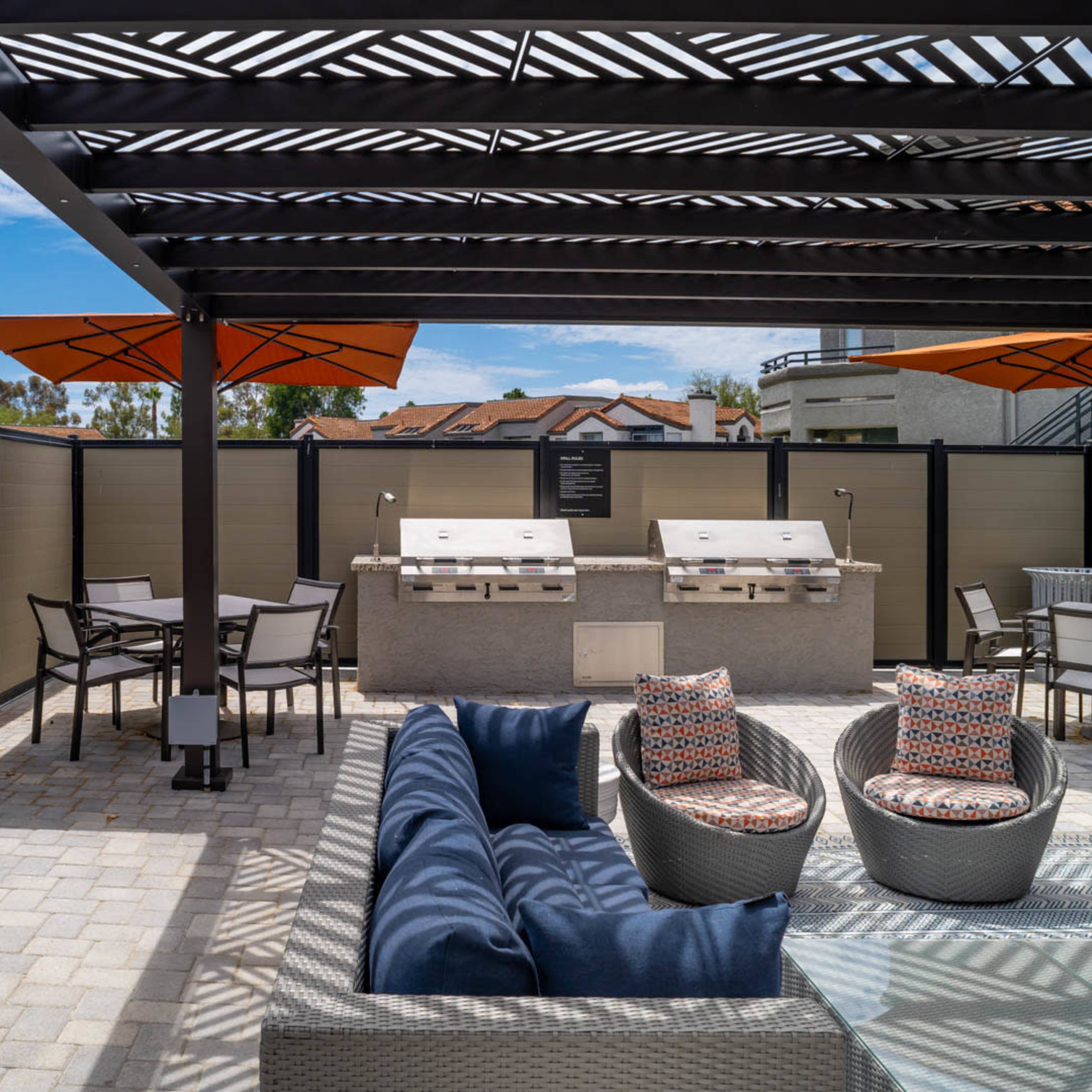 An outdoor grilling area with modern furniture, a stone grill station, and shaded seating under a pergola.
