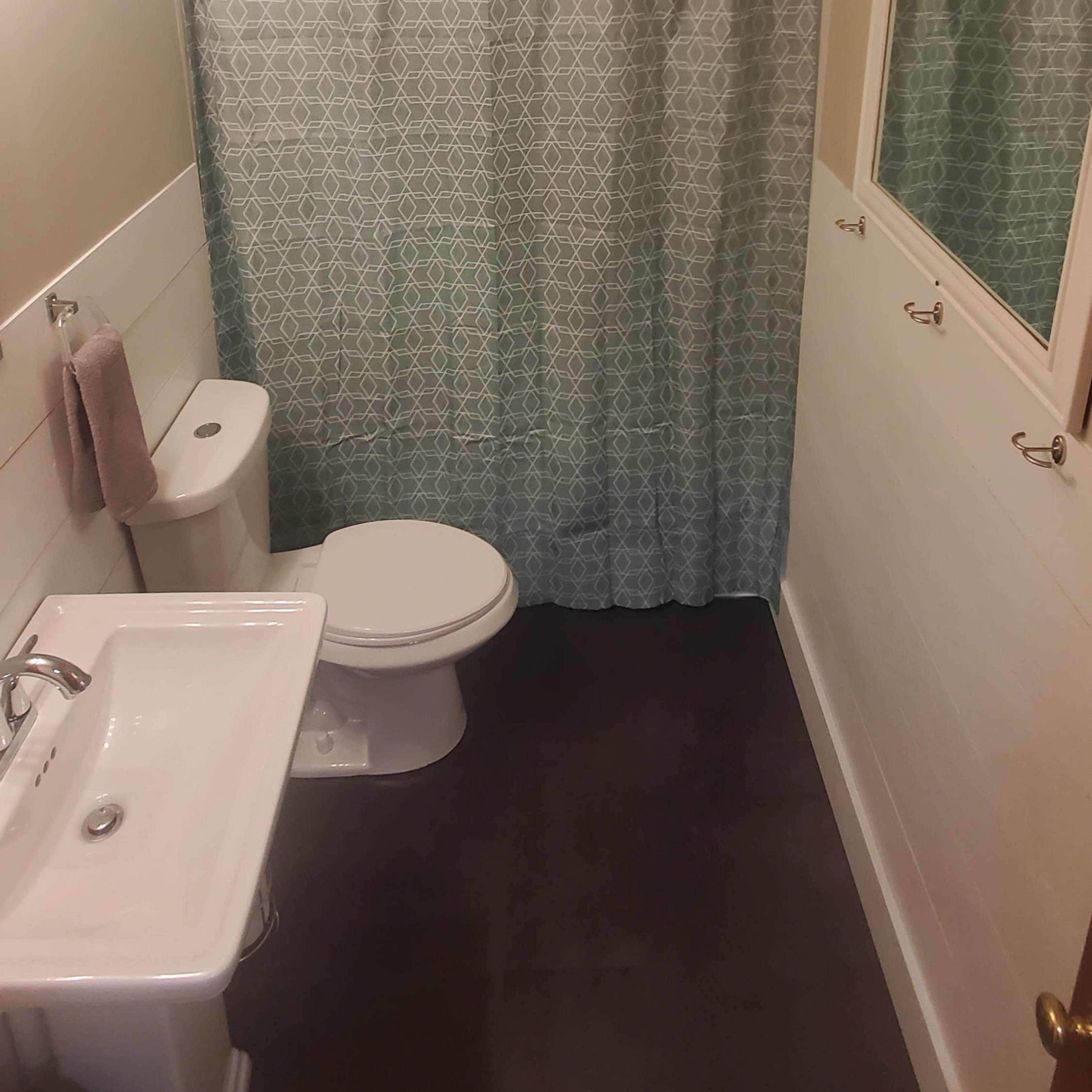 A small bathroom features a toilet, sink, and a shower area separated by a patterned curtain.