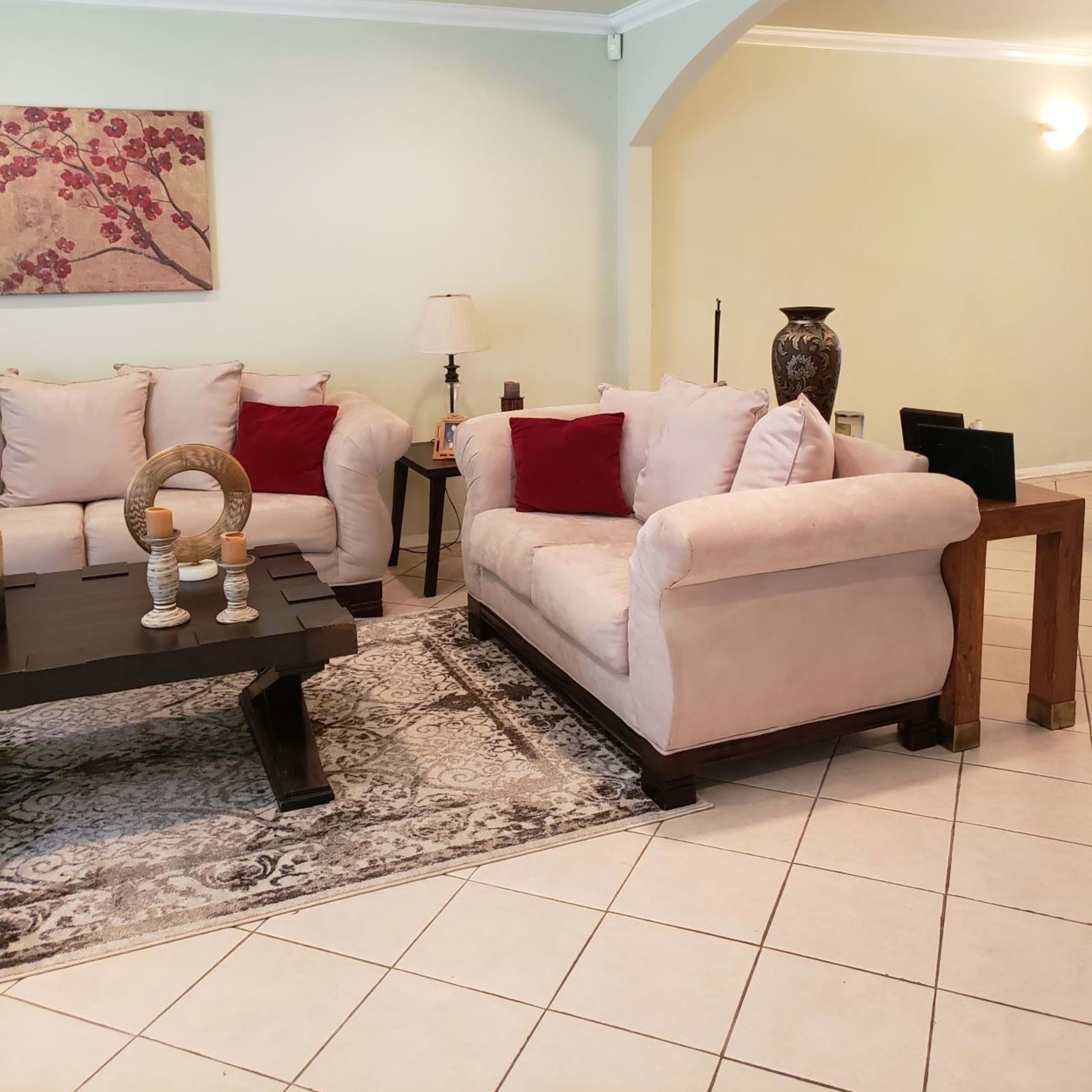 A living room with two beige sofas, a dark wooden coffee table, and a light-colored wall adorned with a floral artwork.