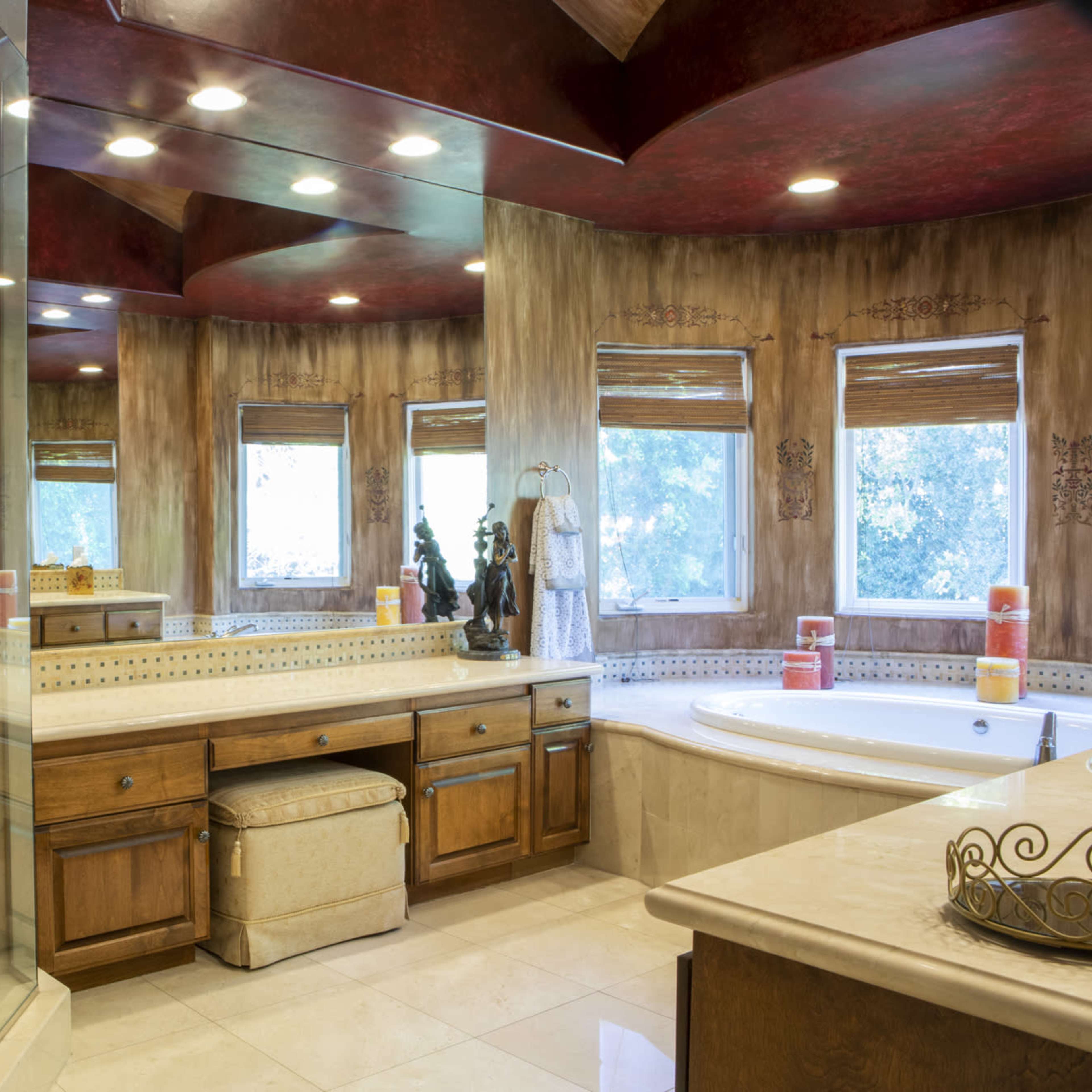 A spacious bathroom featuring a glass-enclosed shower, a large soaking tub, and dual sinks under illuminated coffered ceilings.