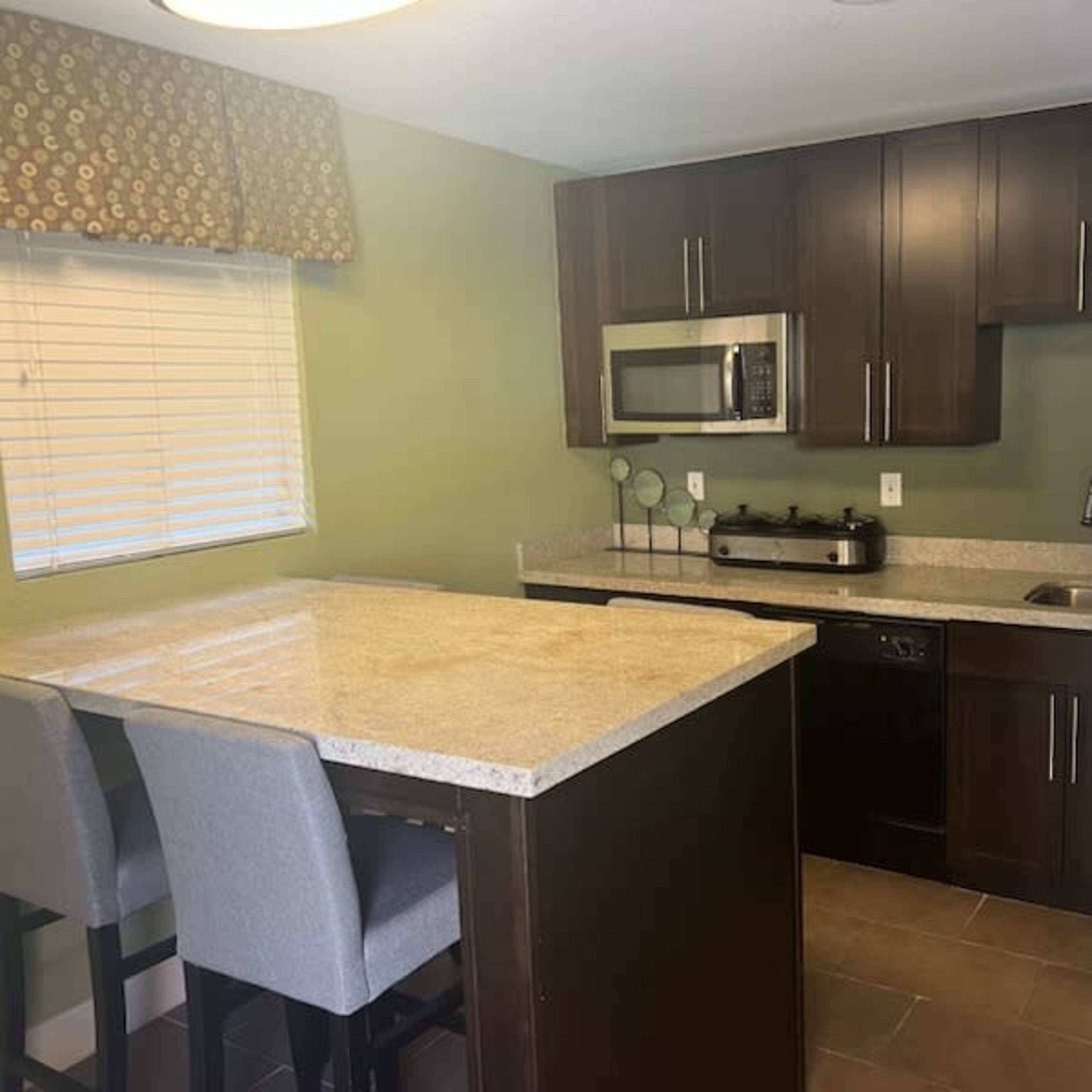 A modern kitchen with dark wood cabinets, stainless steel appliances, and a granite countertop with two bar stools.