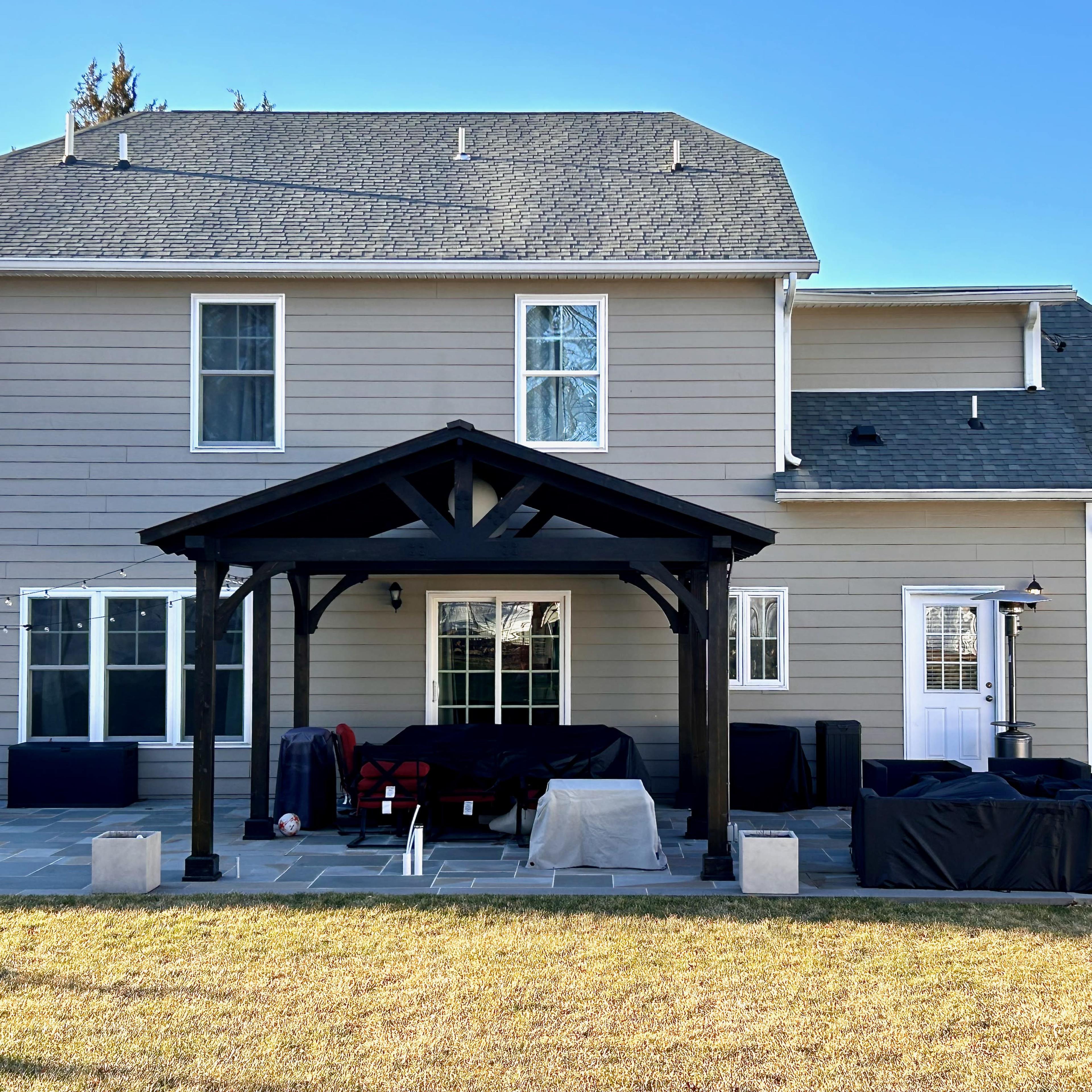 A two-story house with a covered patio, surrounded by a grassy yard and several outdoor furniture pieces covered with protective tarps.