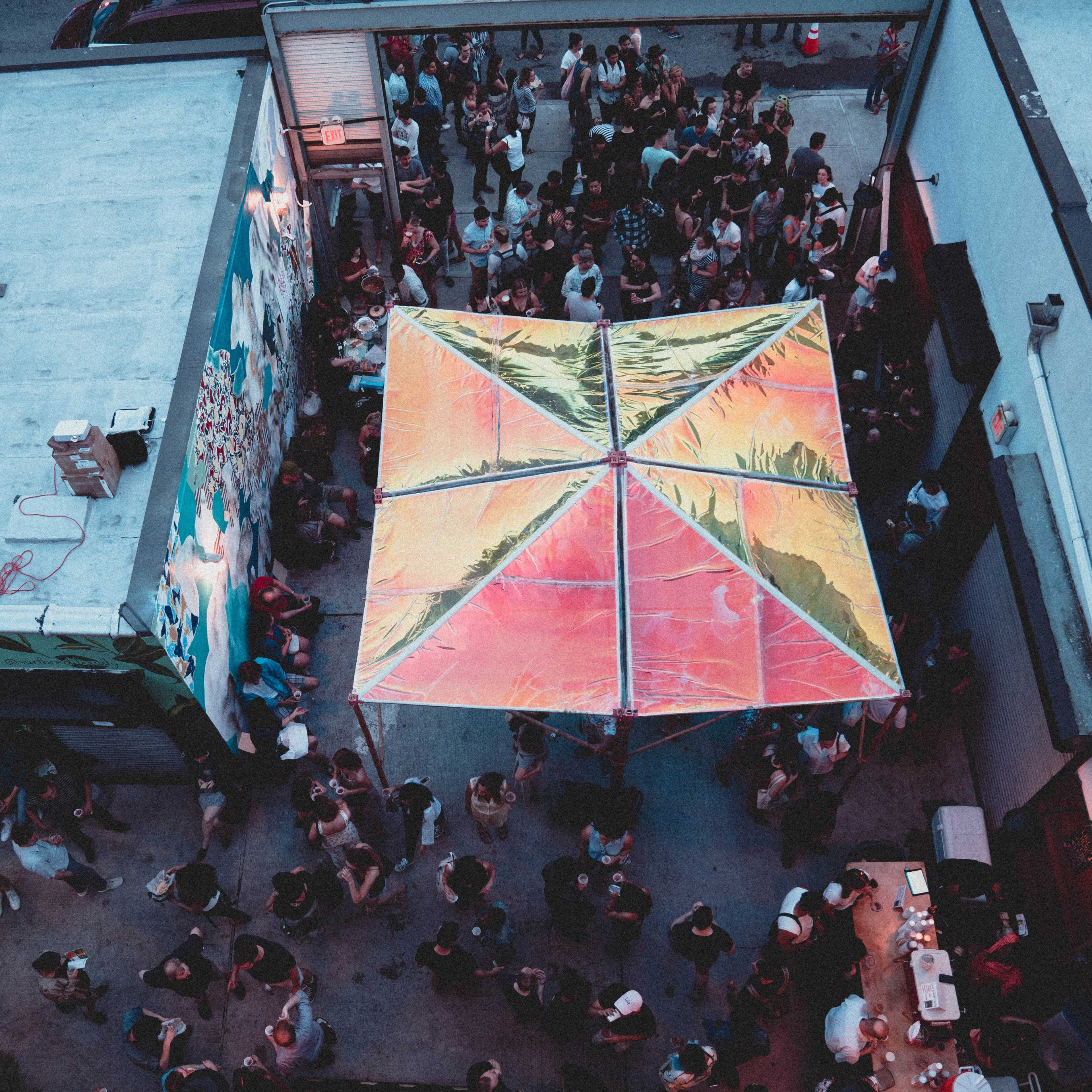Aerial view of a crowded outdoor gathering featuring a large, colorful canopy in the center.