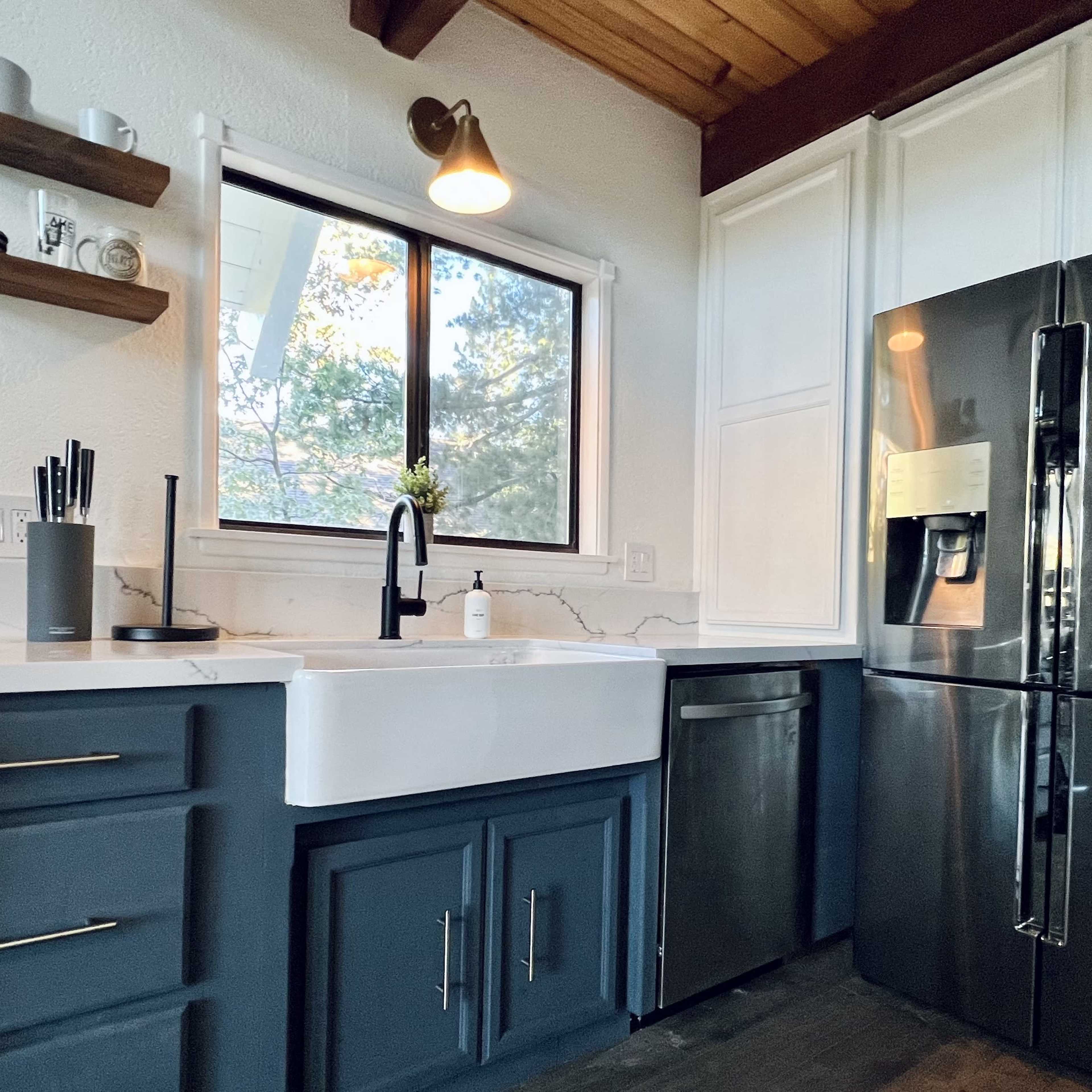 A modern kitchen featuring a farmhouse sink, dark cabinetry, and stainless steel appliances.