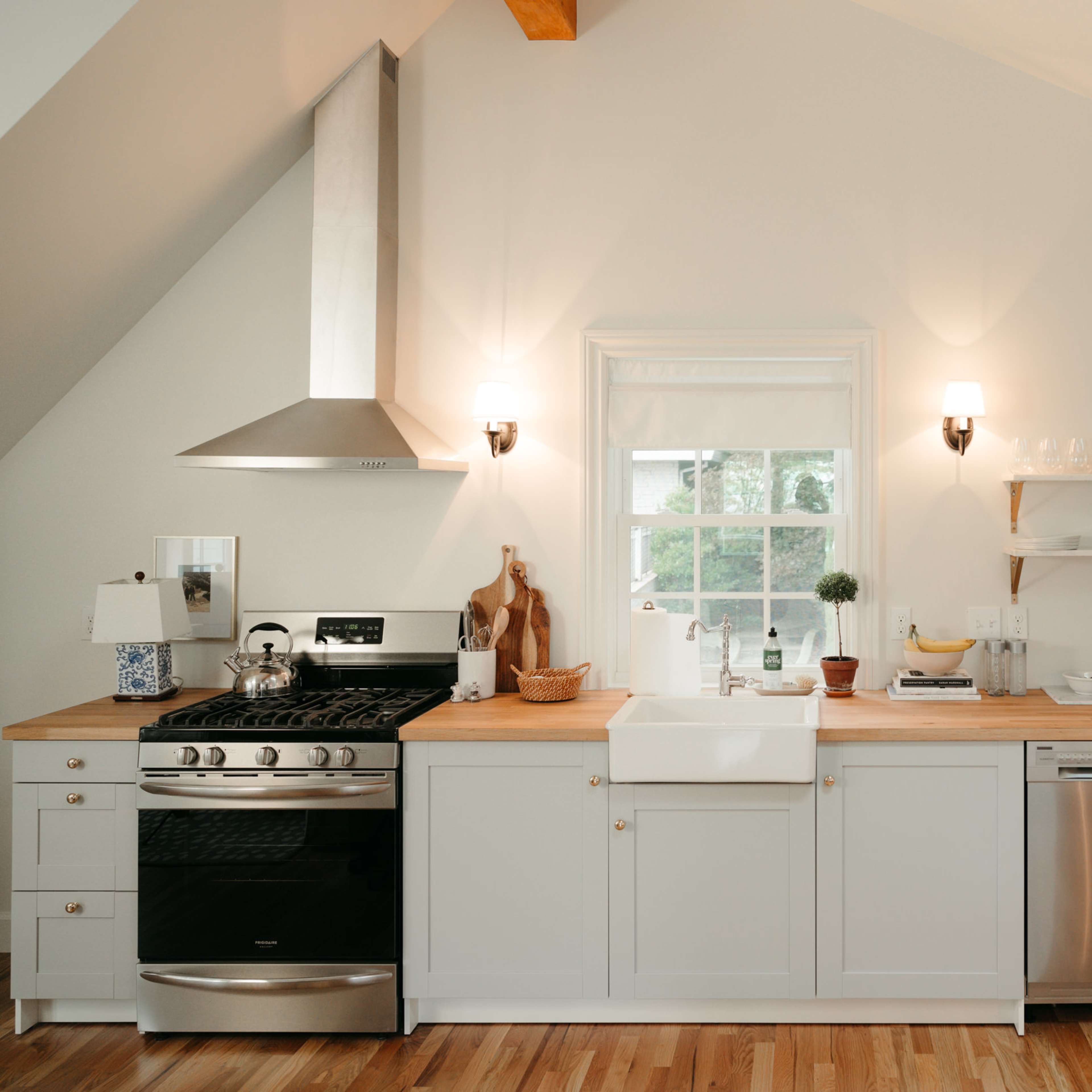 A modern kitchen features white cabinets, a stainless steel refrigerator, and a farmhouse sink beneath a window.