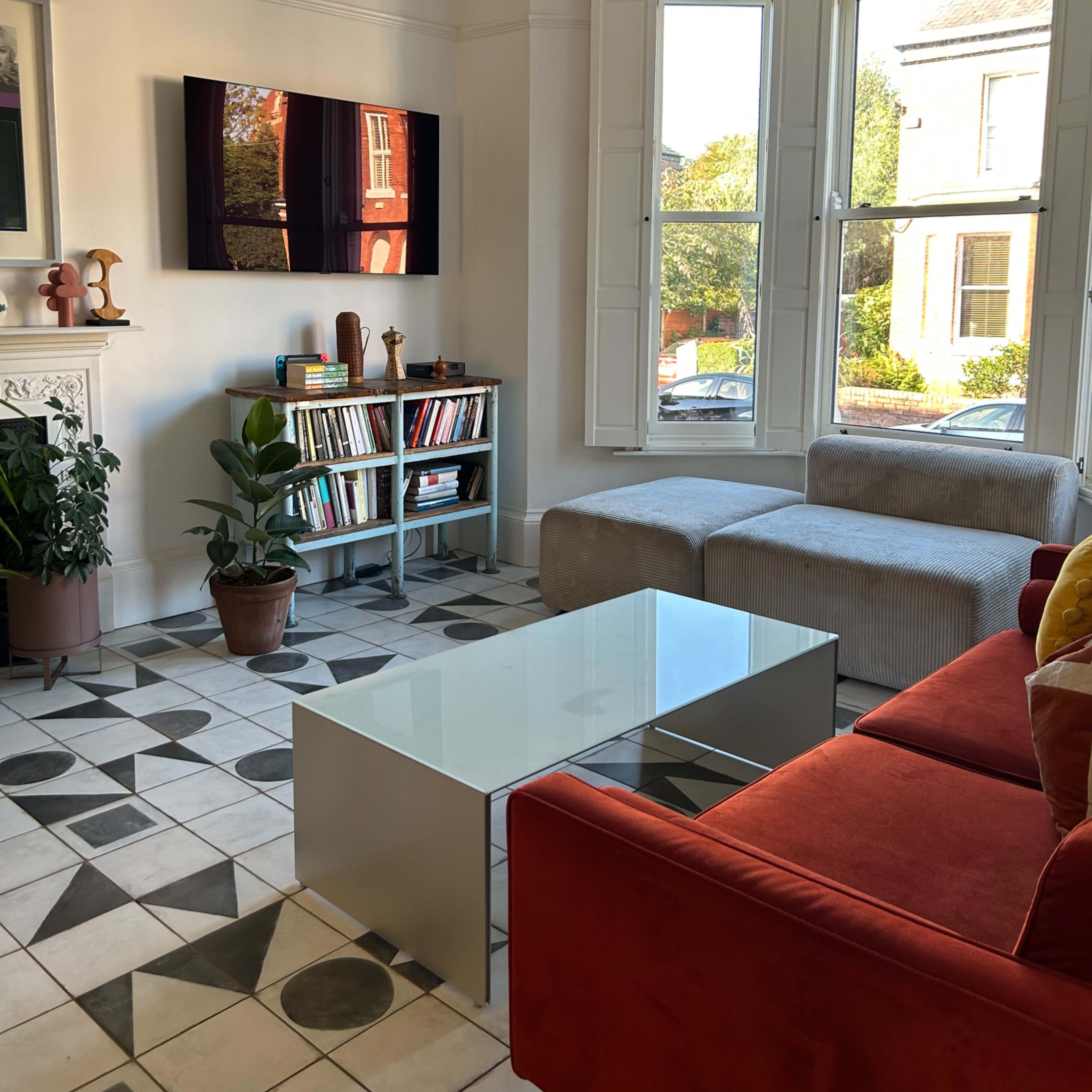 A modern living room with a red sofa, a glass coffee table, and a bookshelf next to large windows that let in natural light.