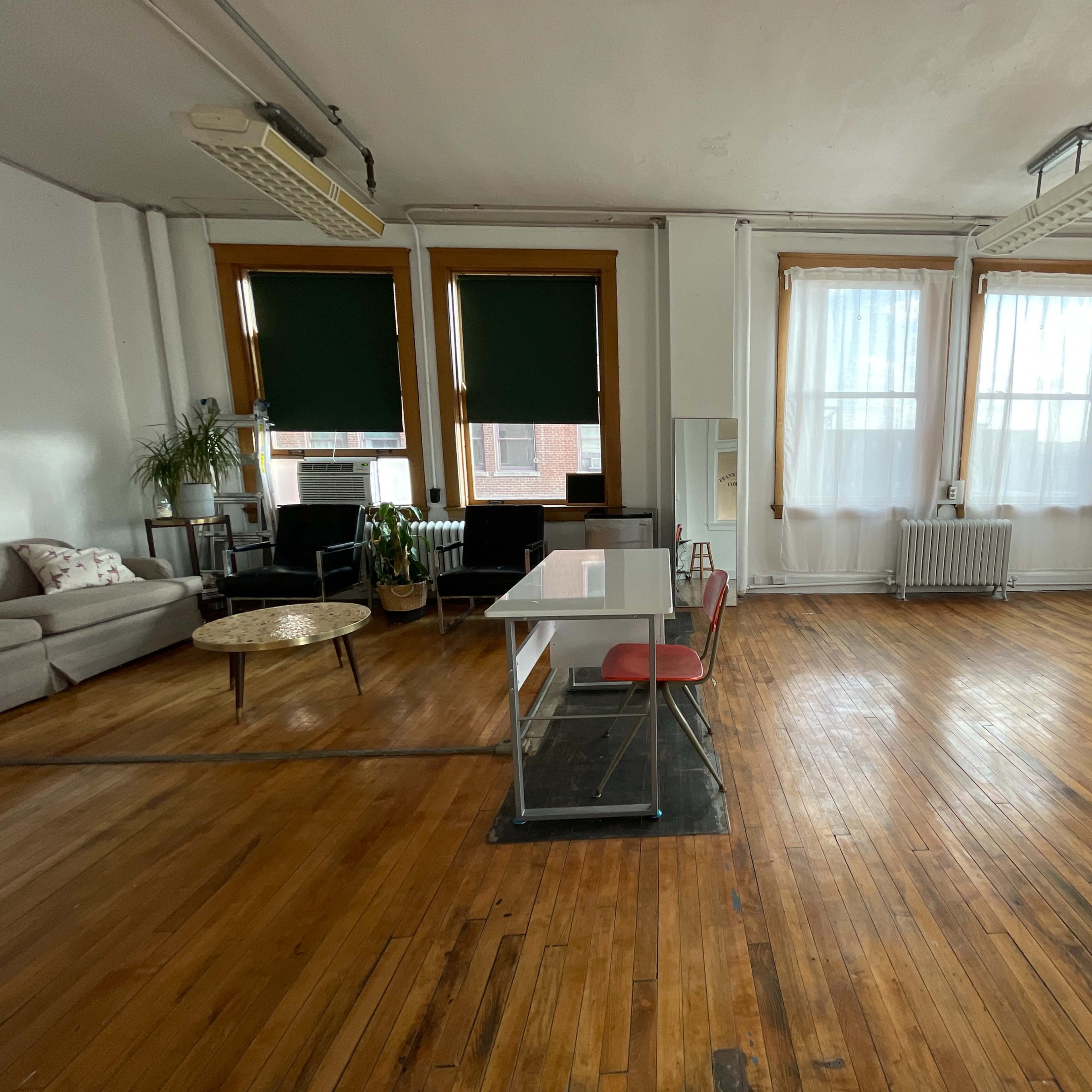 A spacious room with wooden floors, large windows, a glass table, a sofa, and a ladder in the corner.