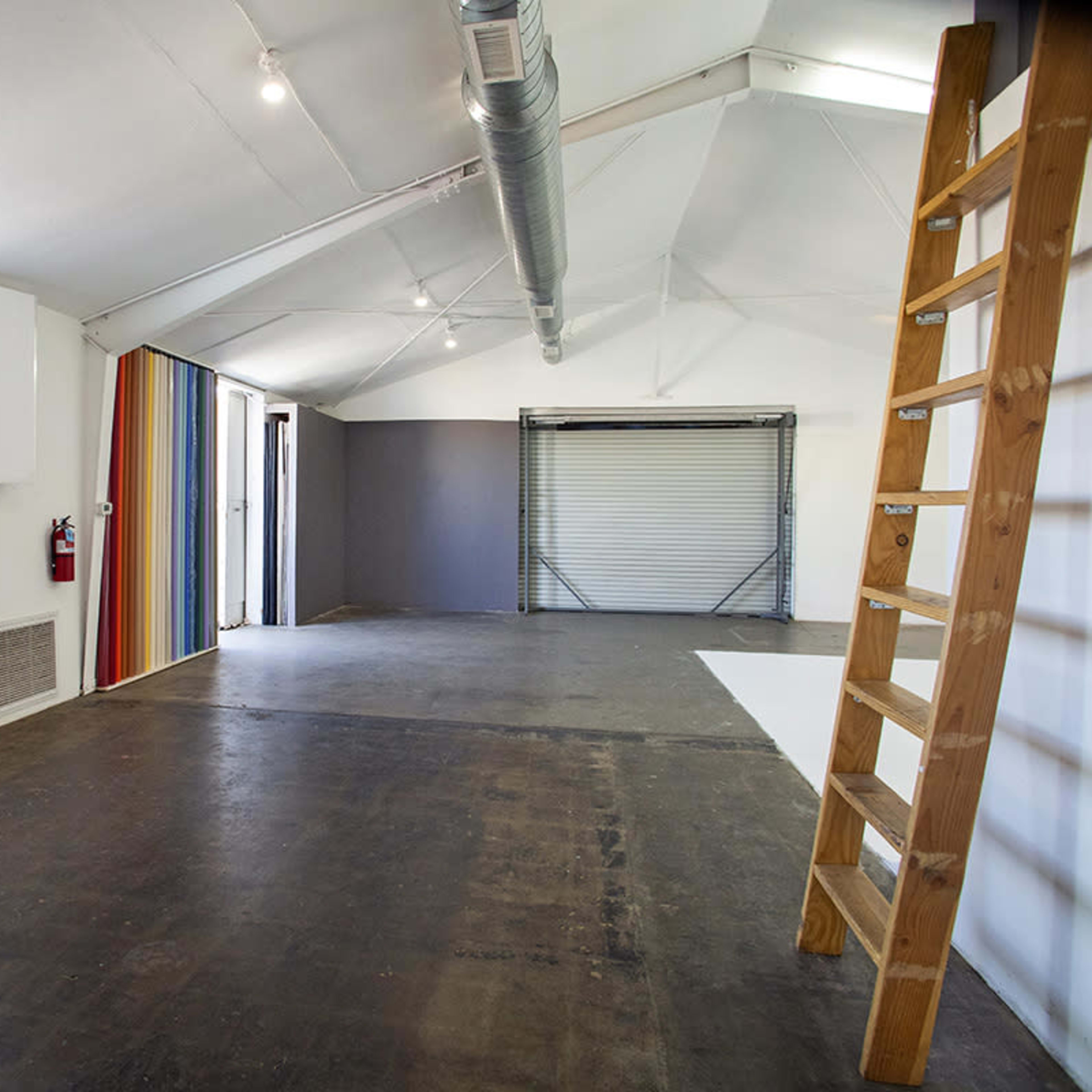 A spacious room with a ladder on the right side, a large window, and colorful striped wall panels.