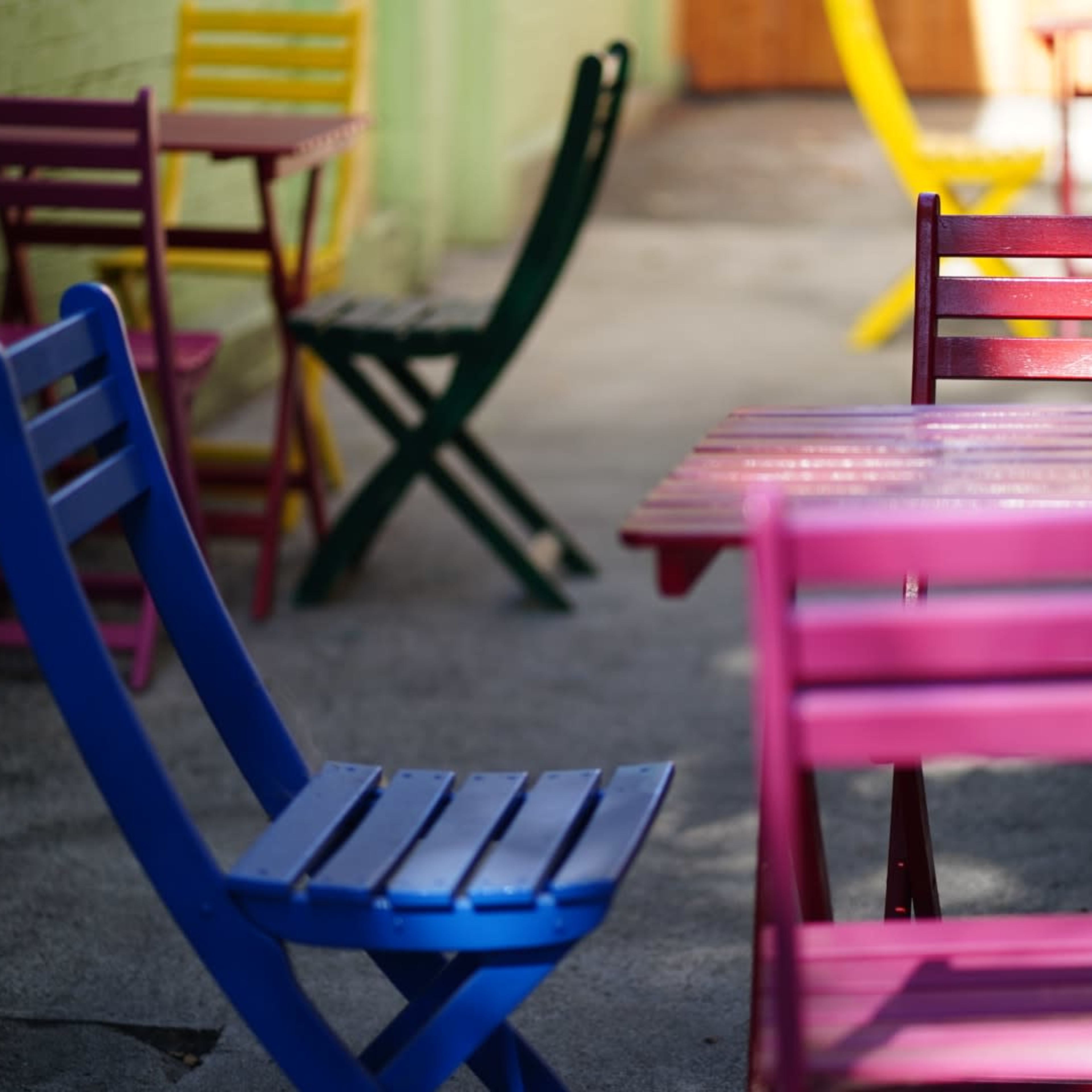Colorful folding chairs and tables are arranged in a narrow outdoor space.