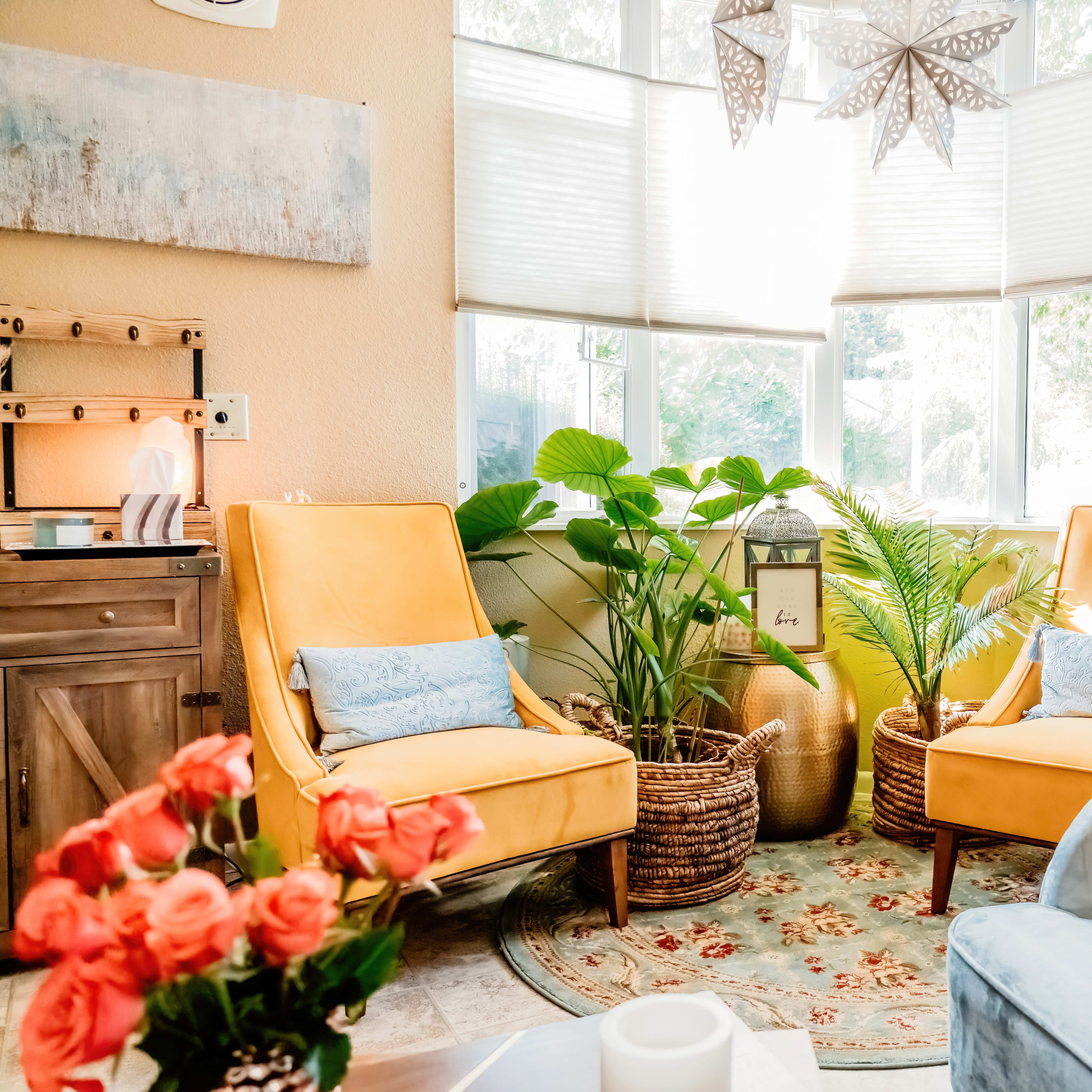 A cozy seating area with two yellow armchairs, a blue couch, and various indoor plants surrounded by natural light.
