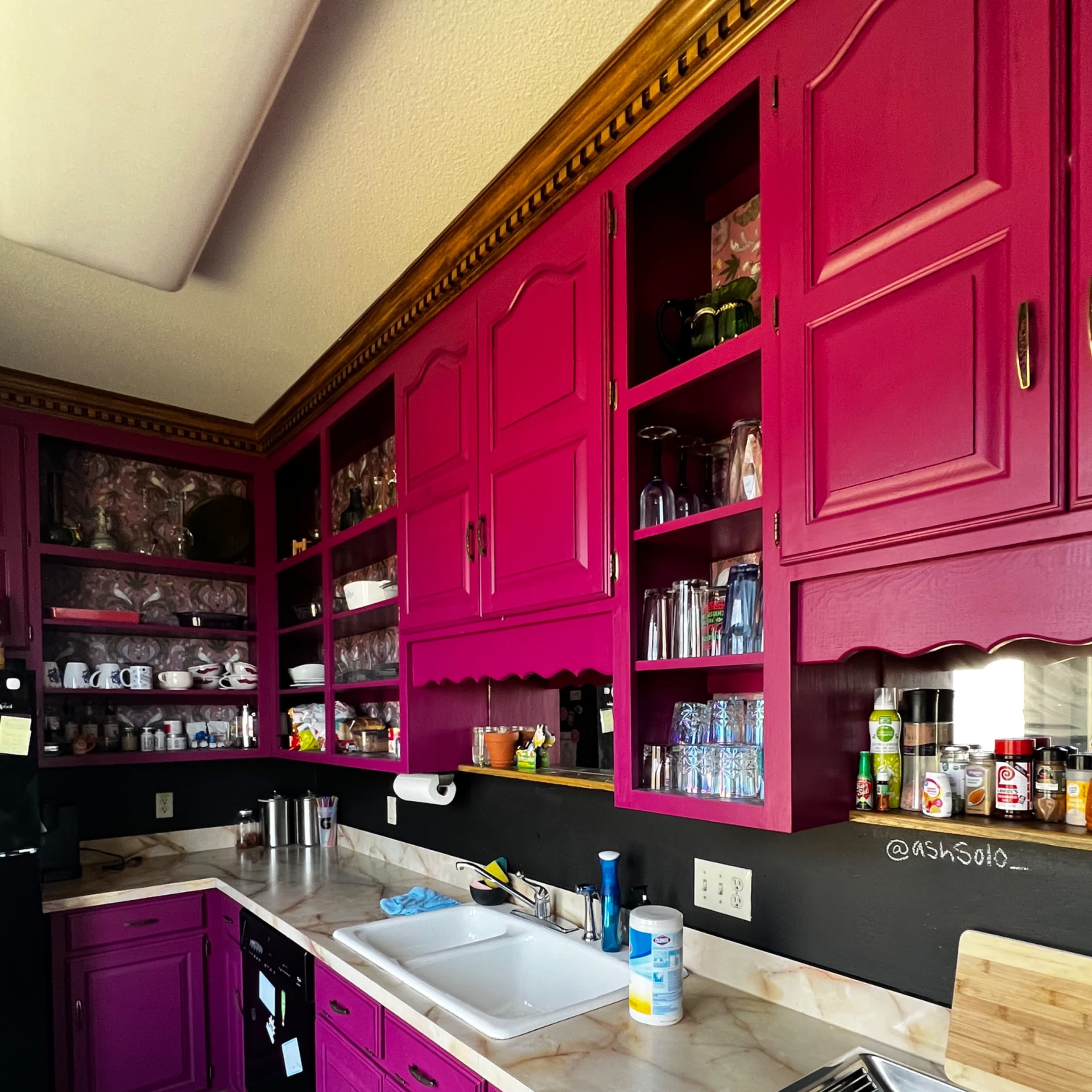 The kitchen features bright pink cabinets and a white countertop with various utensils and appliances visible.