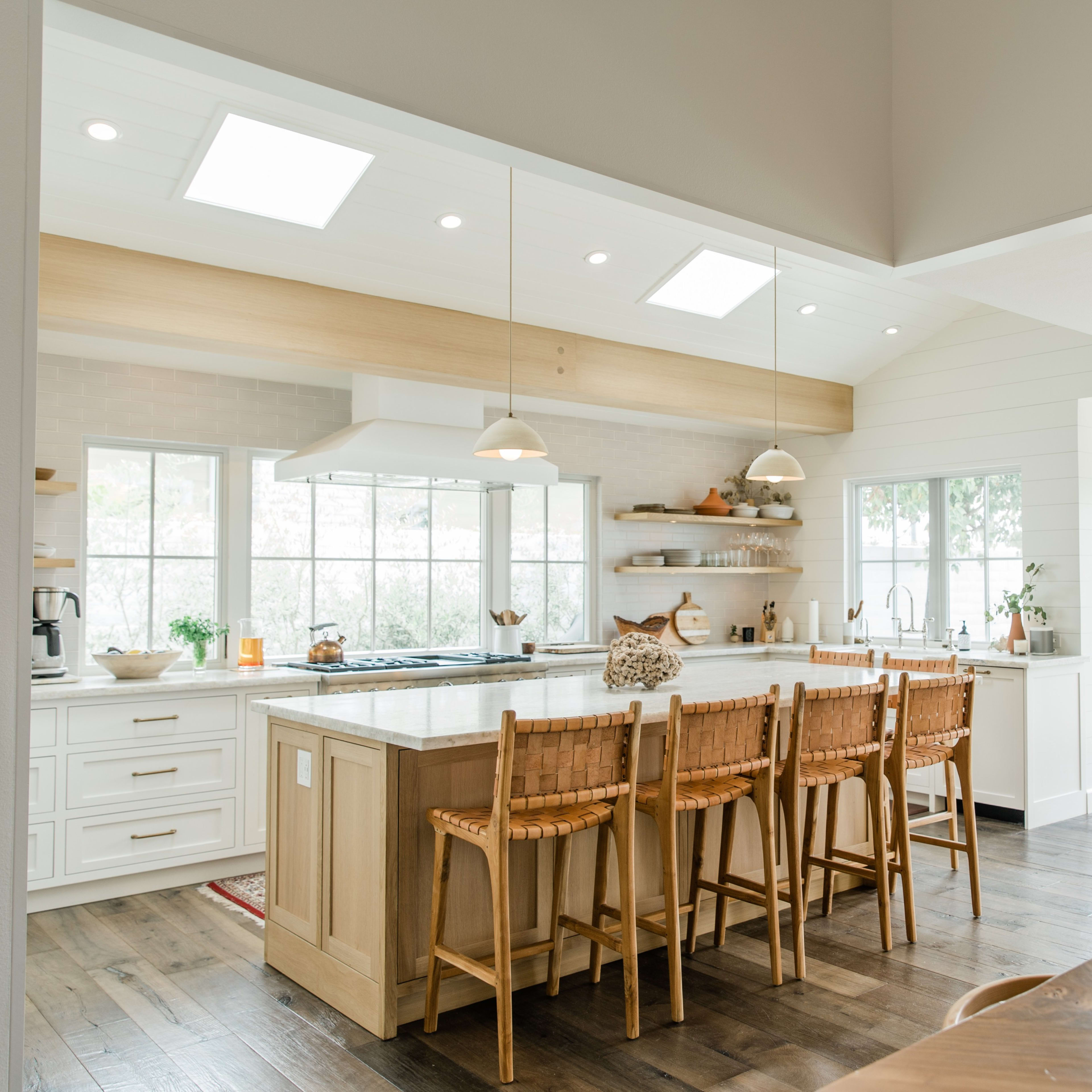 A modern kitchen features an island with seating, large windows, and white cabinets.