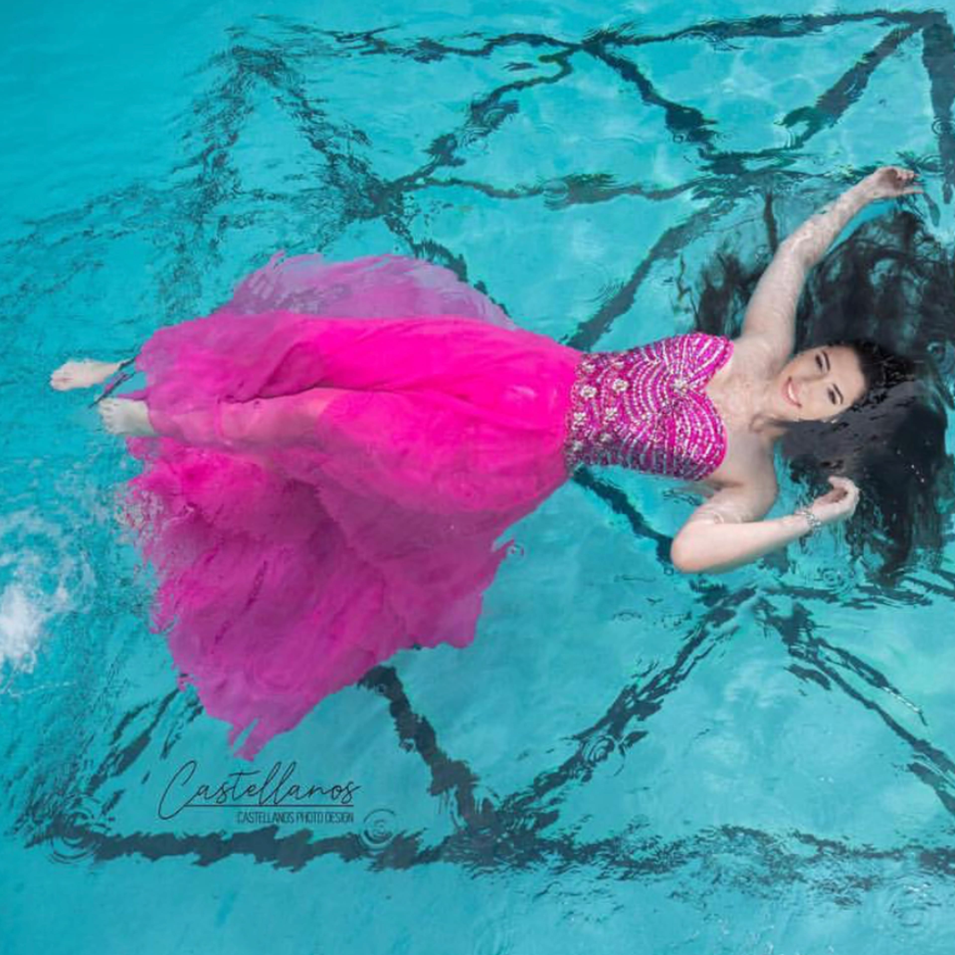 A woman in a pink dress floats on the surface of a pool, with a star-shaped pattern visible on the bottom.