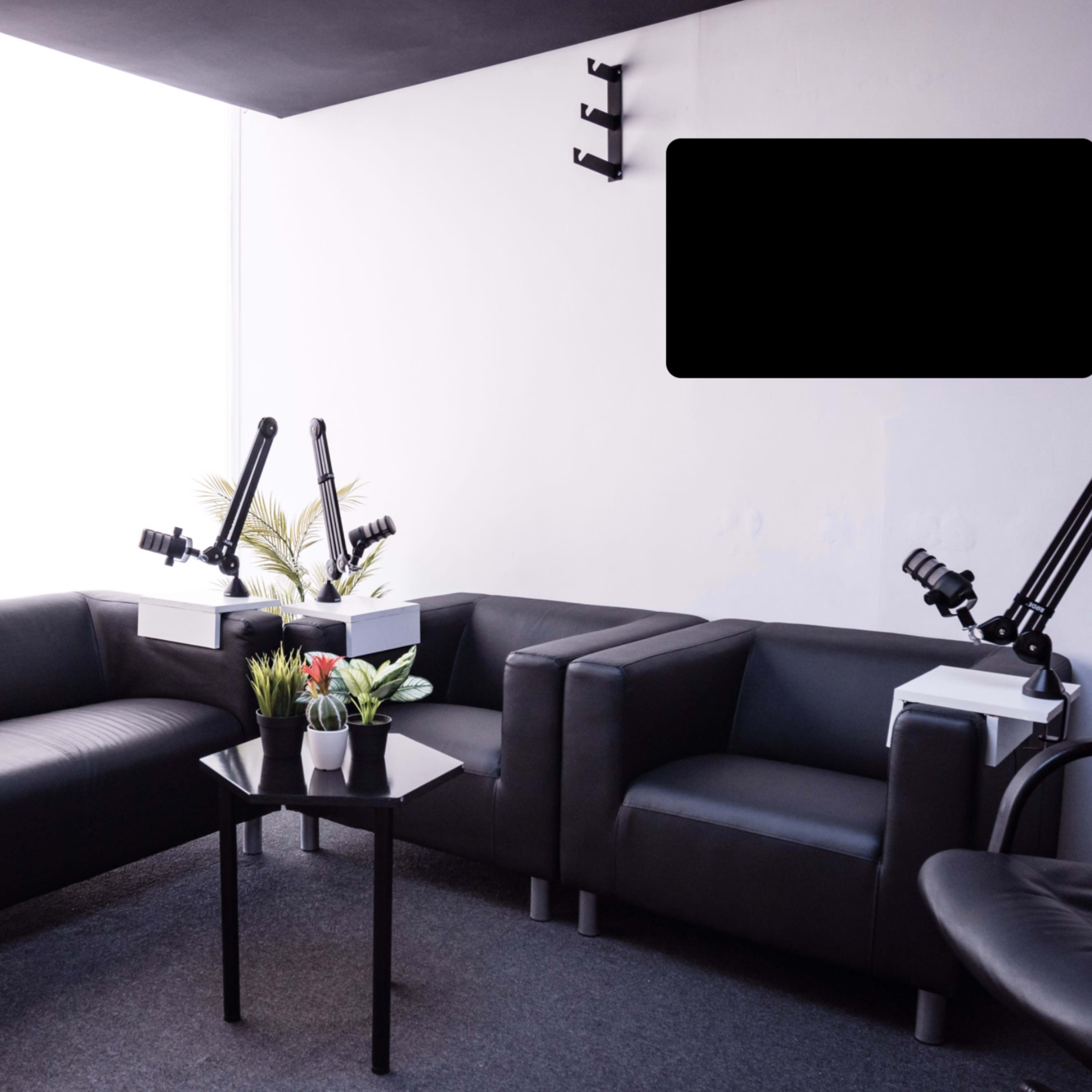 A minimalist seating area with two black sofas, a small black table, and adjustable arm lamps, situated in a well-lit room with large windows.