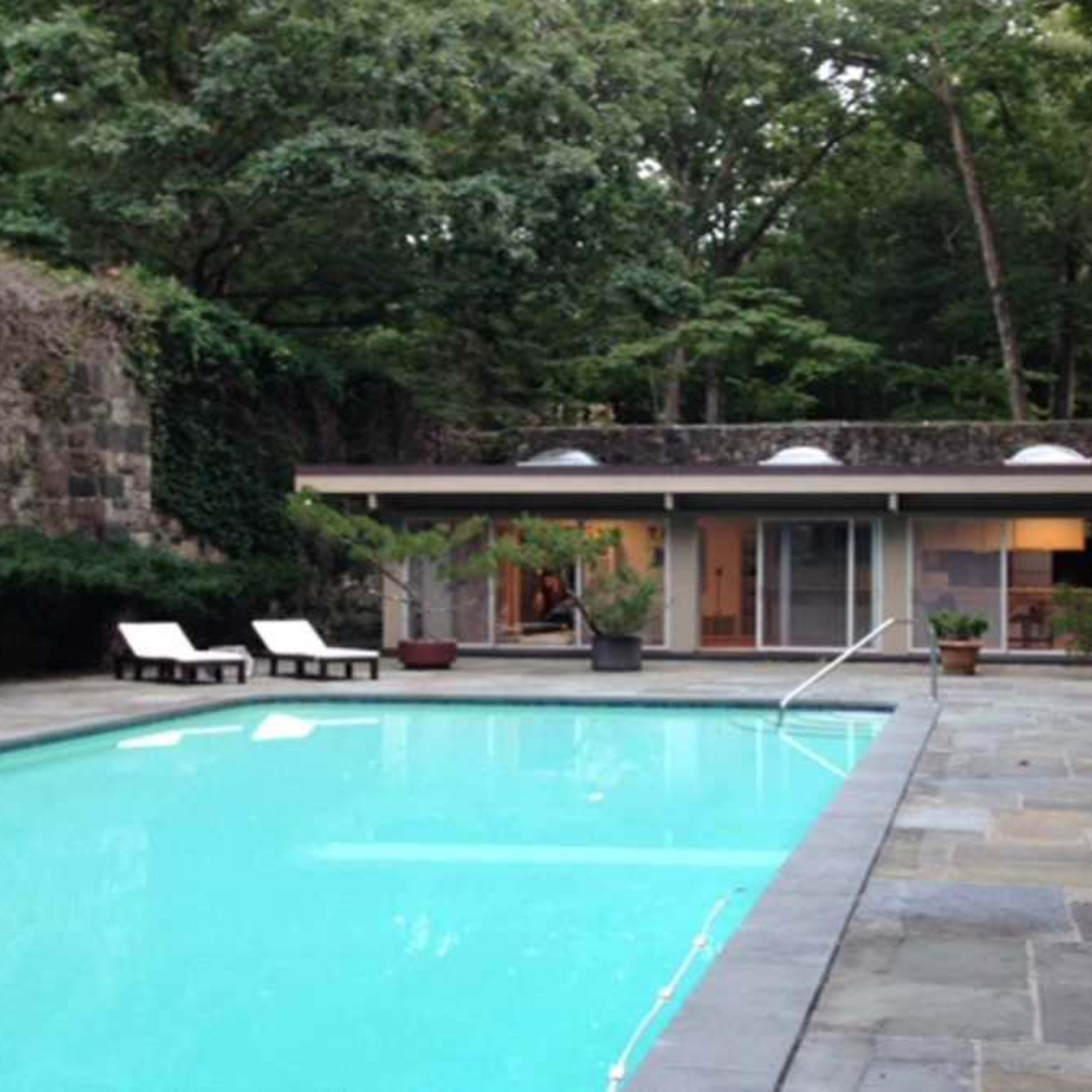 A modern house beside a swimming pool, surrounded by trees and rock formations.