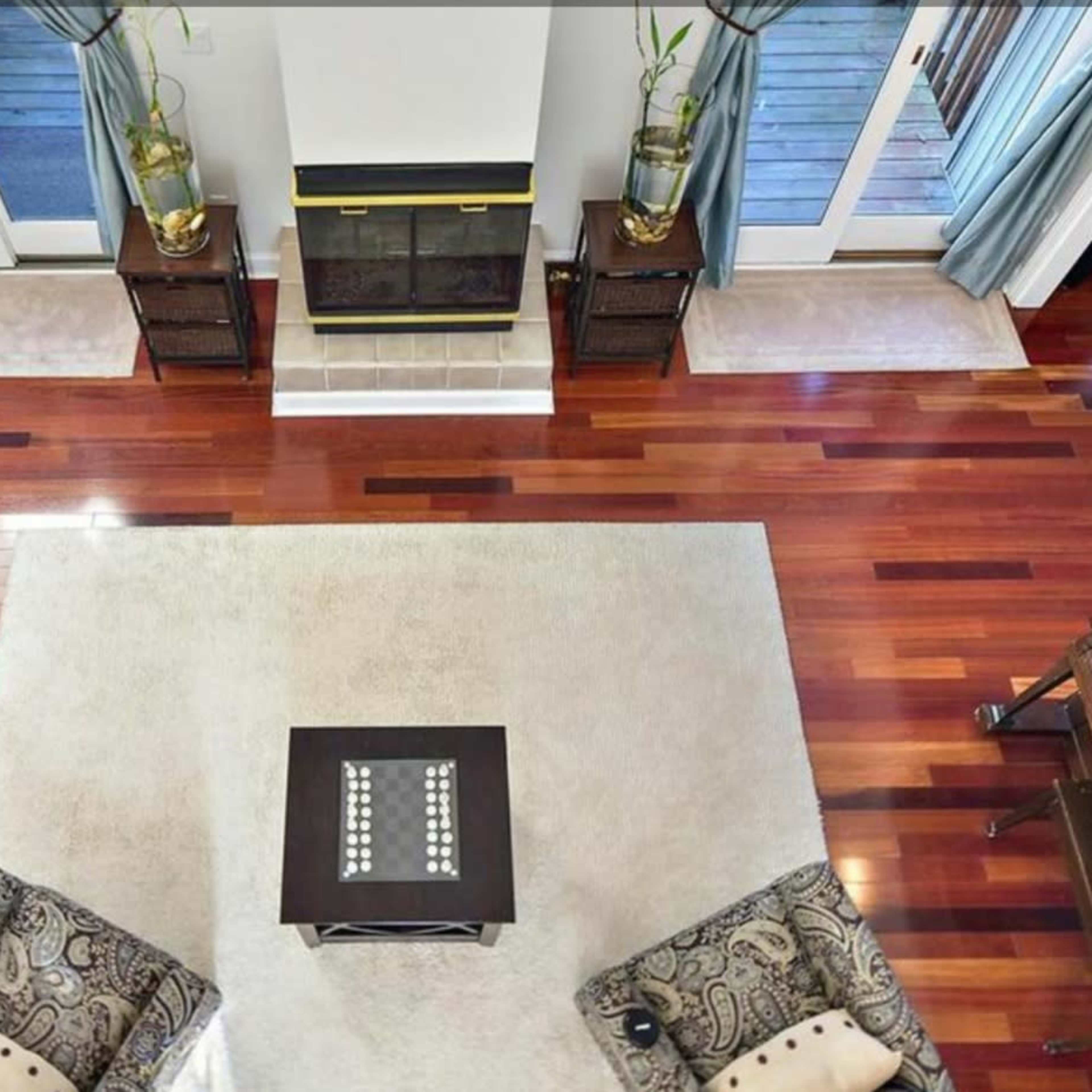 A spacious living room with hardwood floors, a central area rug, two patterned chairs, and a fireplace flanked by sliding glass doors.