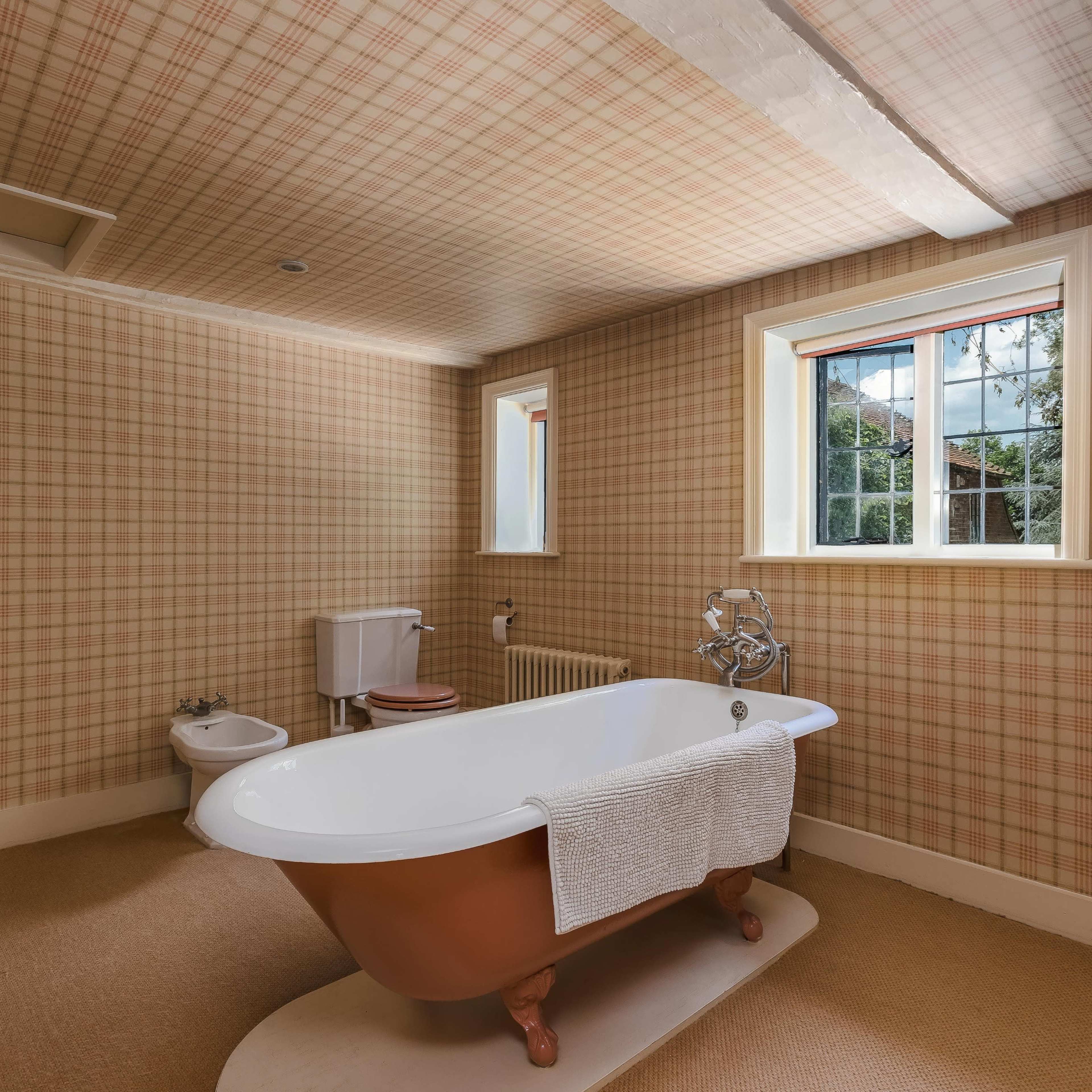 A bathroom featuring a clawfoot bathtub, a toilet, and a window with patterned wallpaper.