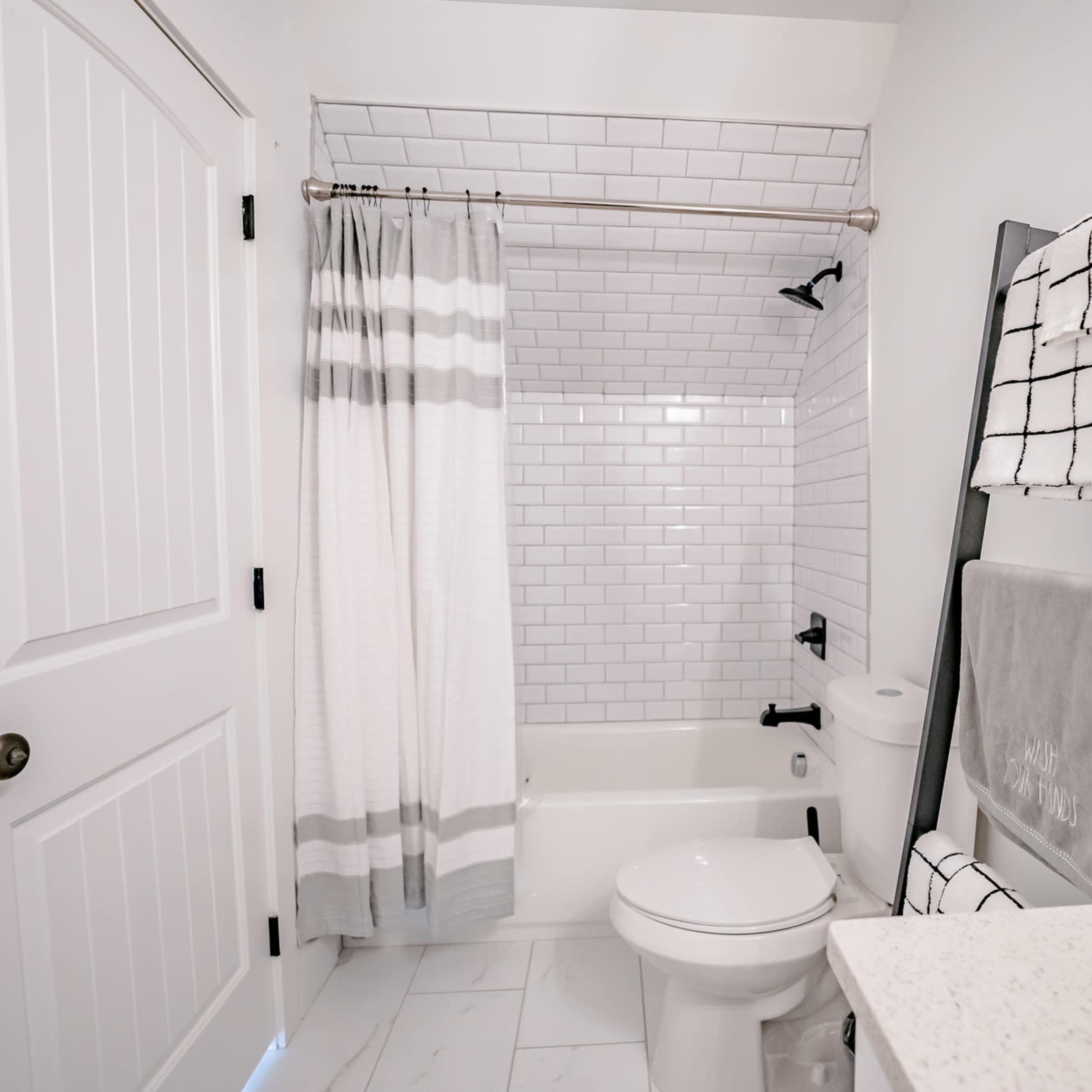 A clean, modern bathroom featuring a bathtub with a shower, white subway tile walls, and a towel rack.