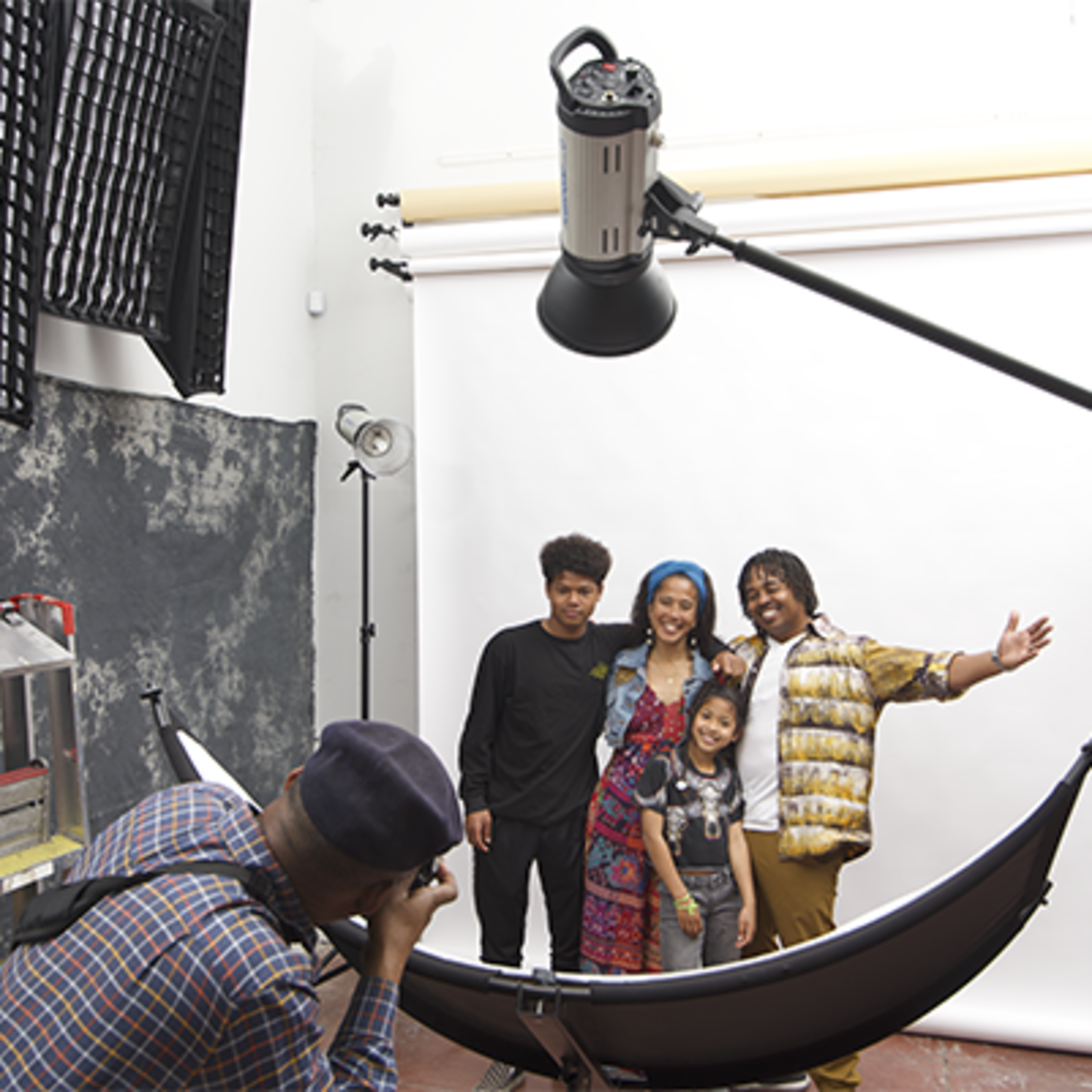 A photographer captures a group of four people posing in a studio with a large softbox and a backdrop.