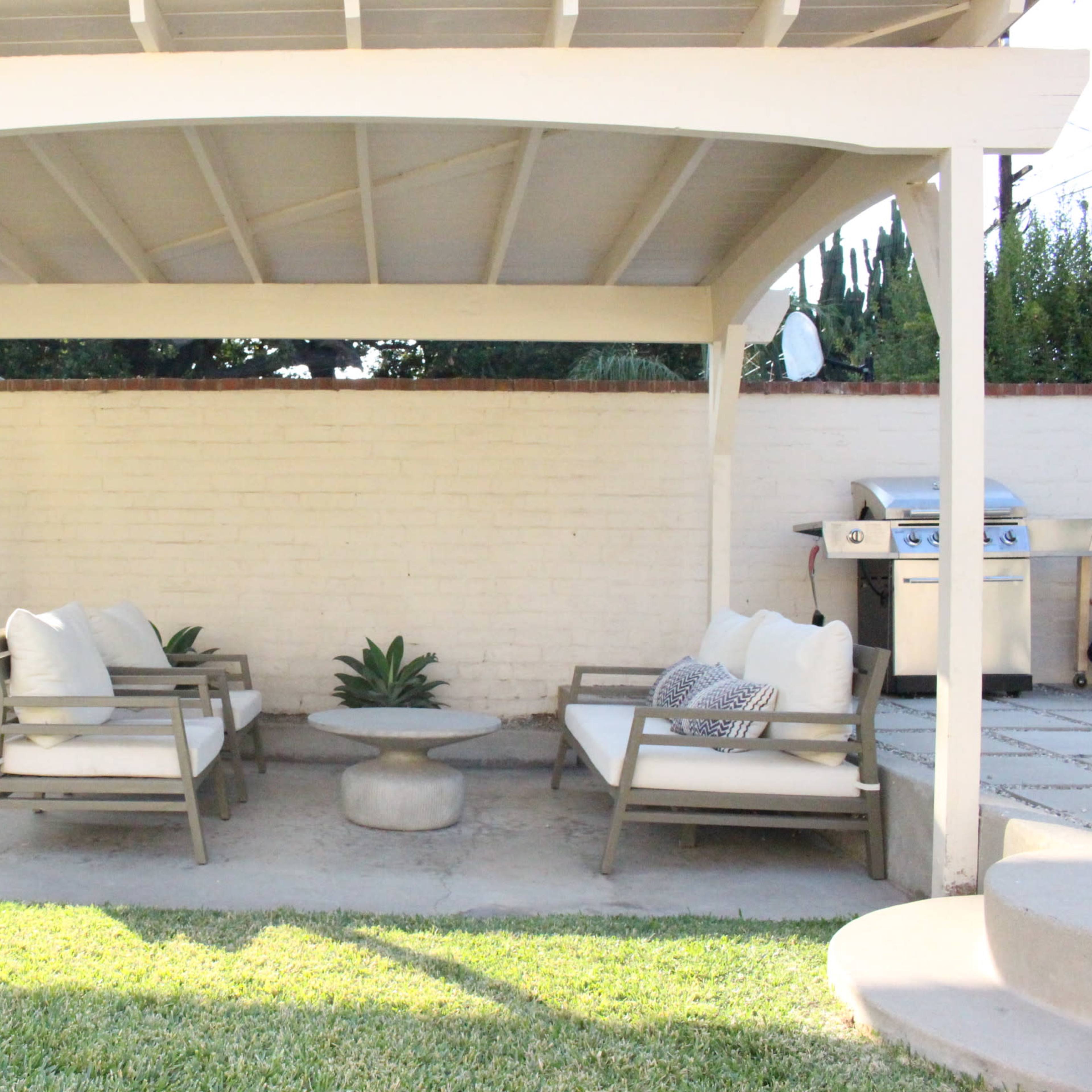 A covered outdoor seating area with two sofas, a coffee table, and a grill in the background.