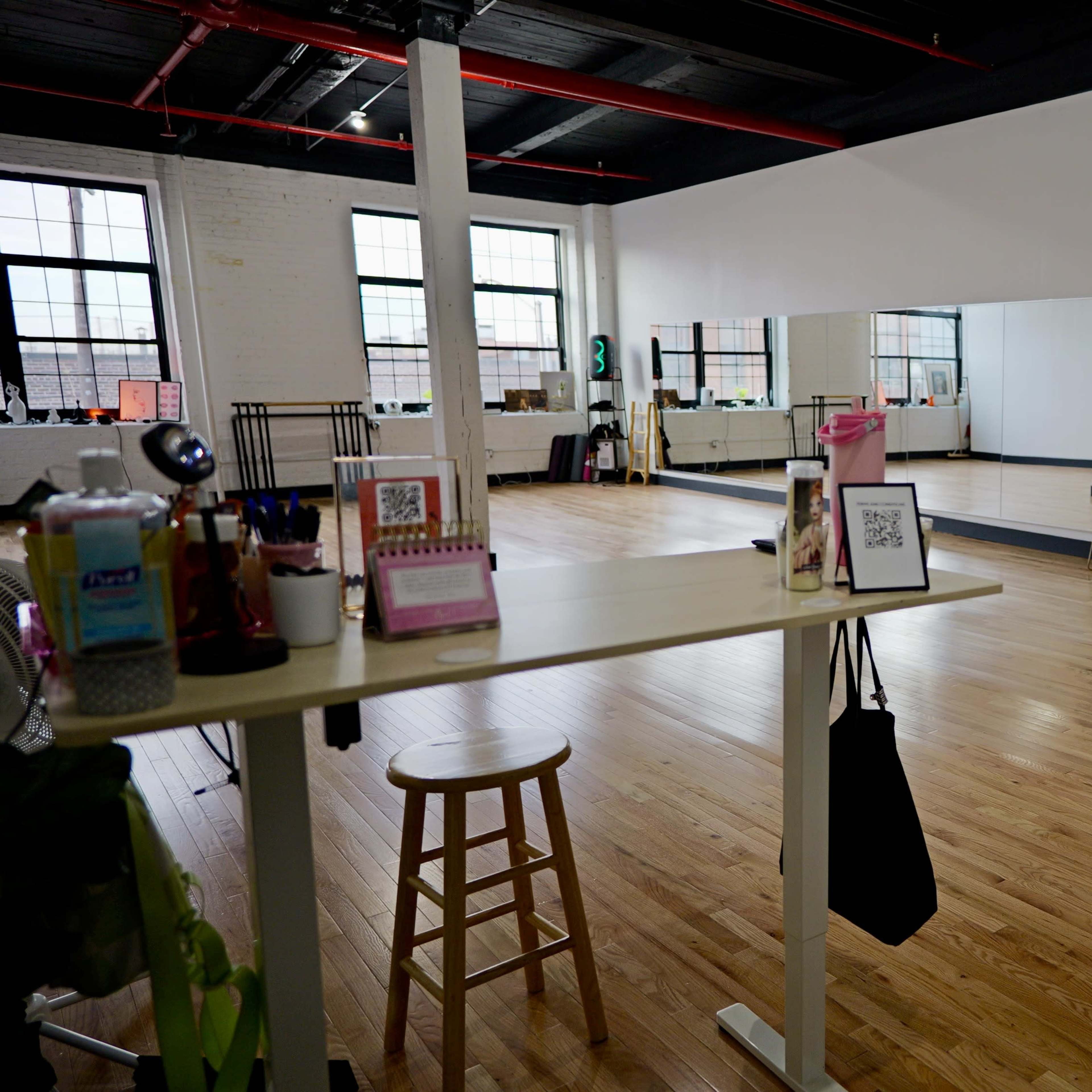 A spacious, well-lit dance studio with wooden floors, mirrors, and a small stage setup at one end.