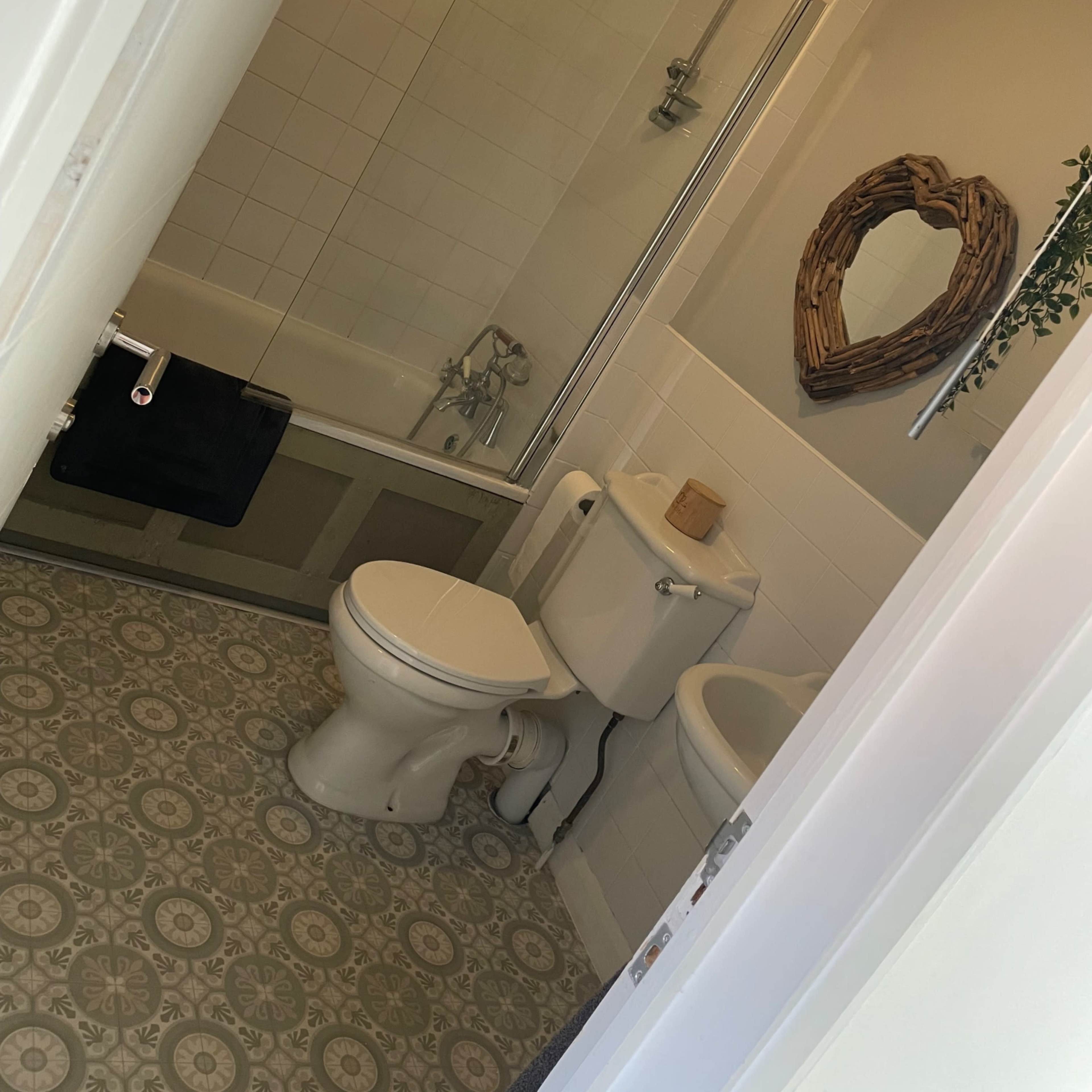 A bathroom with a bathtub, toilet, sink, and patterned floor tiles, viewed from an open doorway.