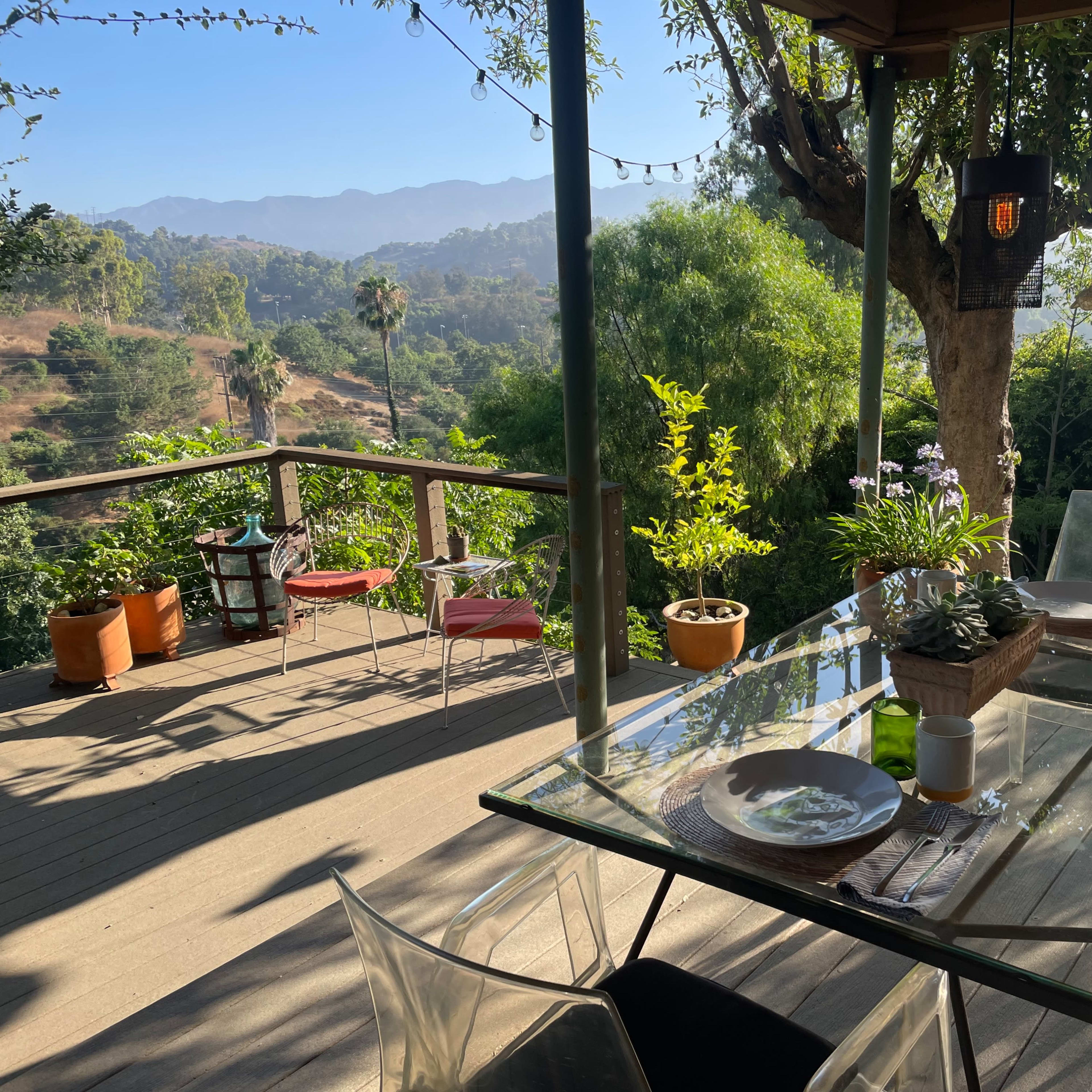 A clear table set for a meal on a deck overlooking a lush hillside with distant mountains.