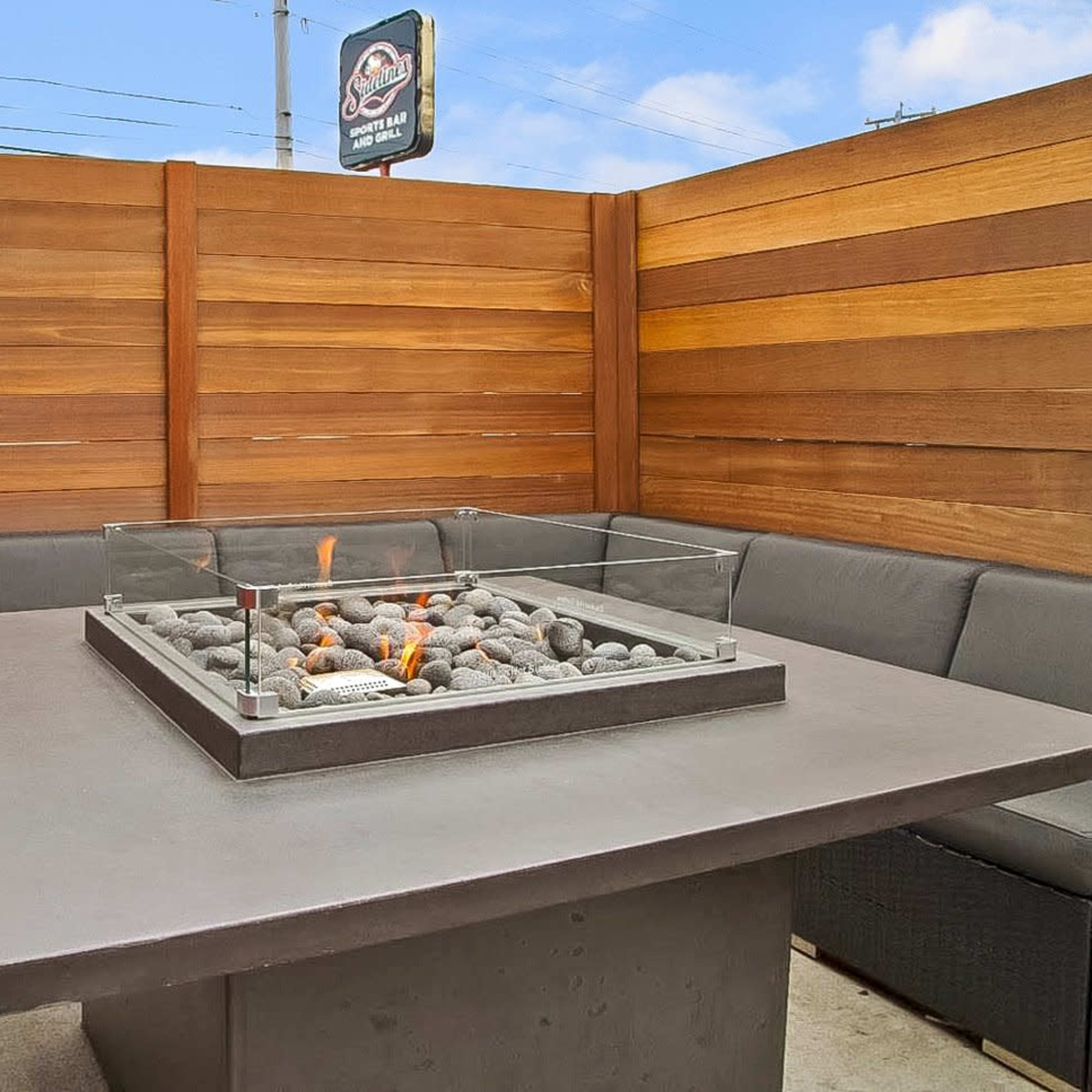 A patio setup featuring a modern fire pit surrounded by gray seating and wooden privacy panels.