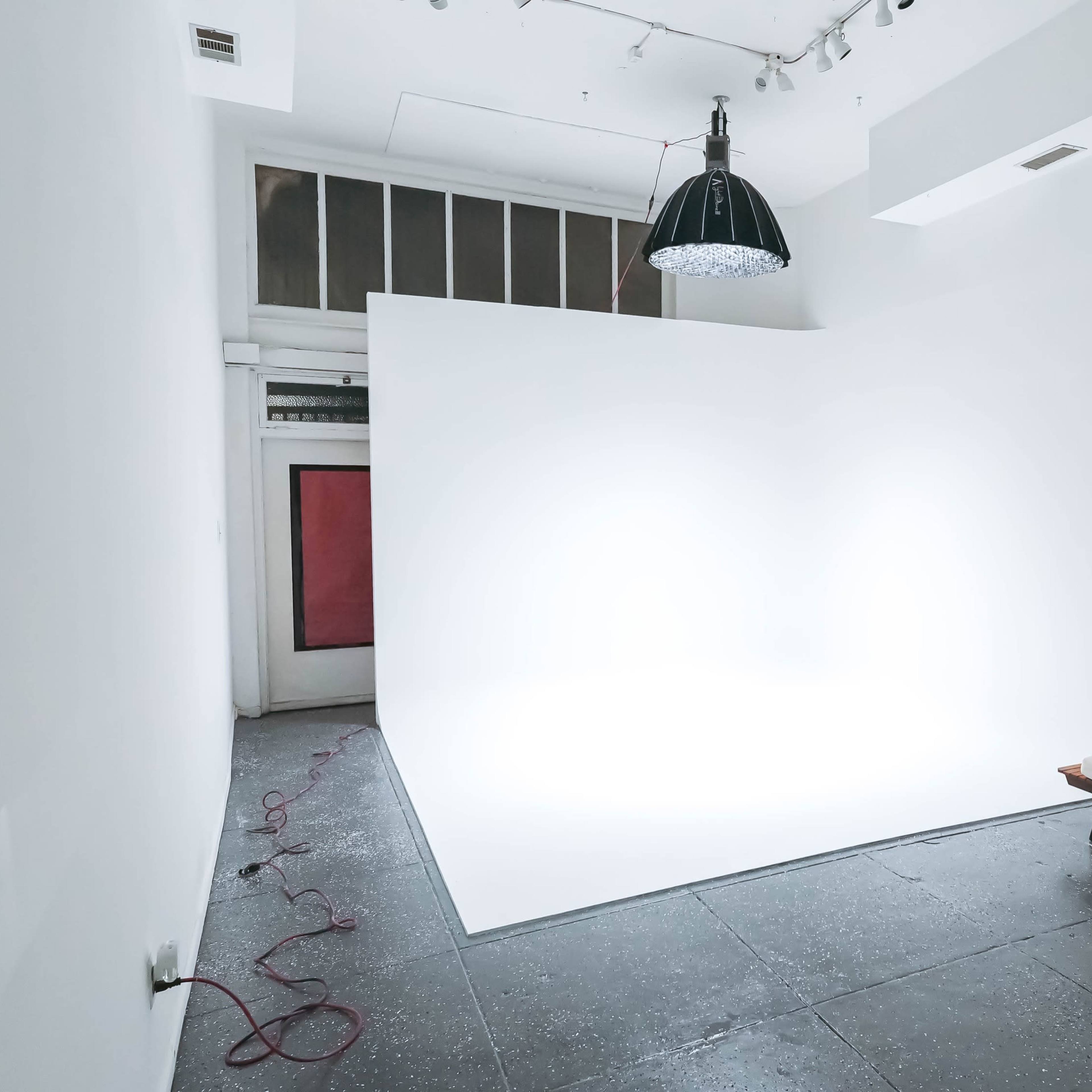A minimalist interior features a bright white backdrop, a wooden bench, and a pendant light in a spacious room.