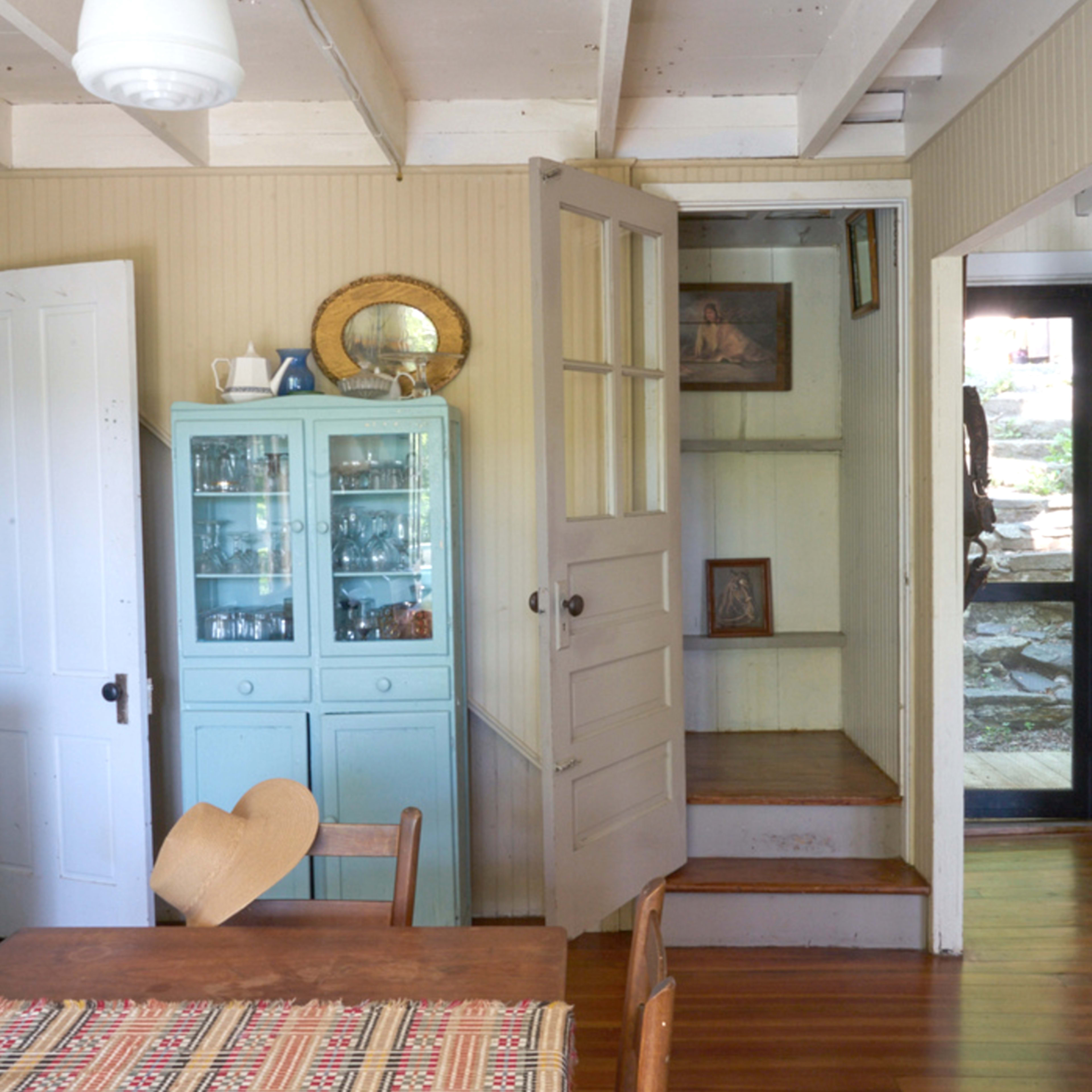A light-filled room with wooden flooring, a dining table, a glass-fronted cabinet, and doorways leading to other areas.