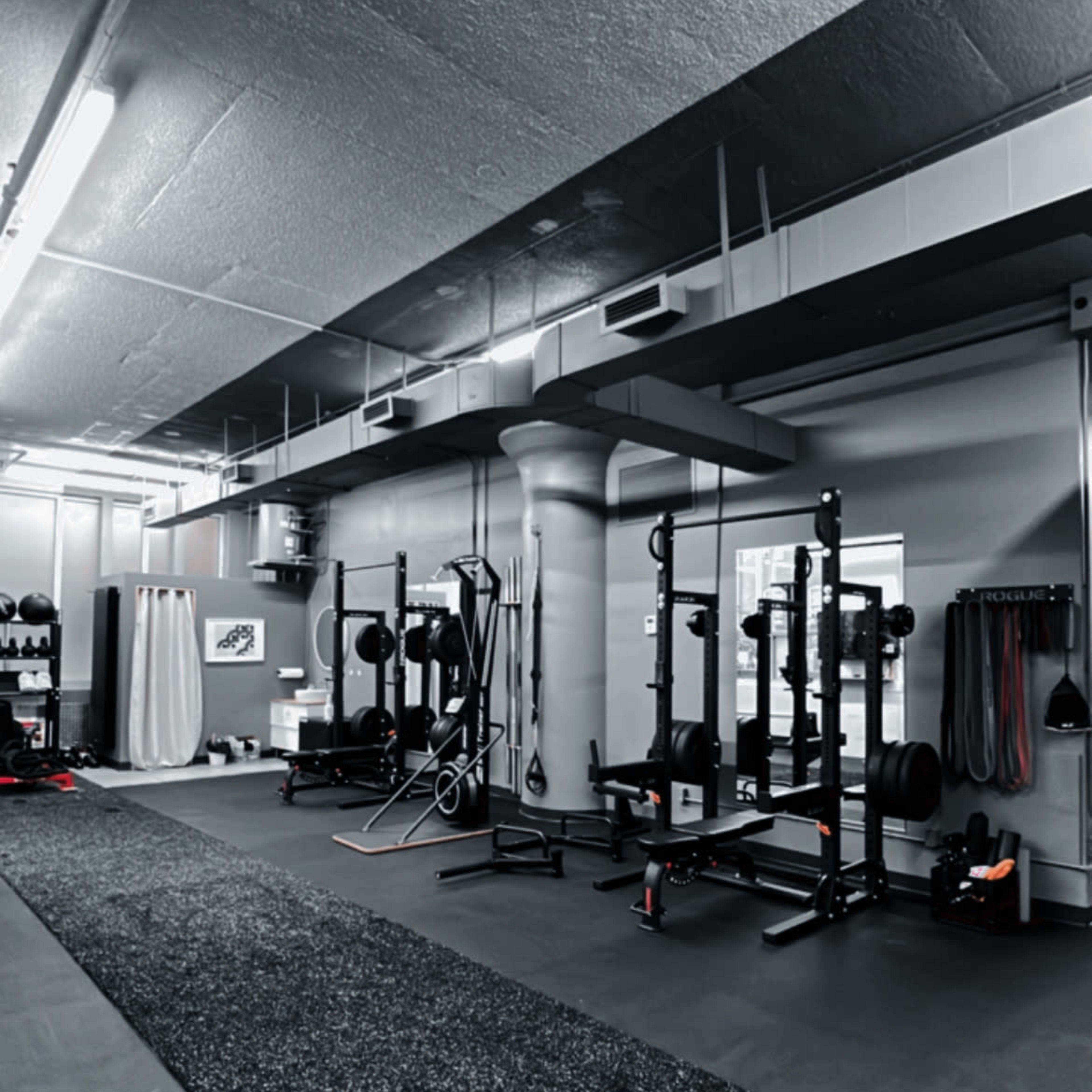 An empty gym interior with various weightlifting equipment arranged along the walls and a rubber flooring surface.