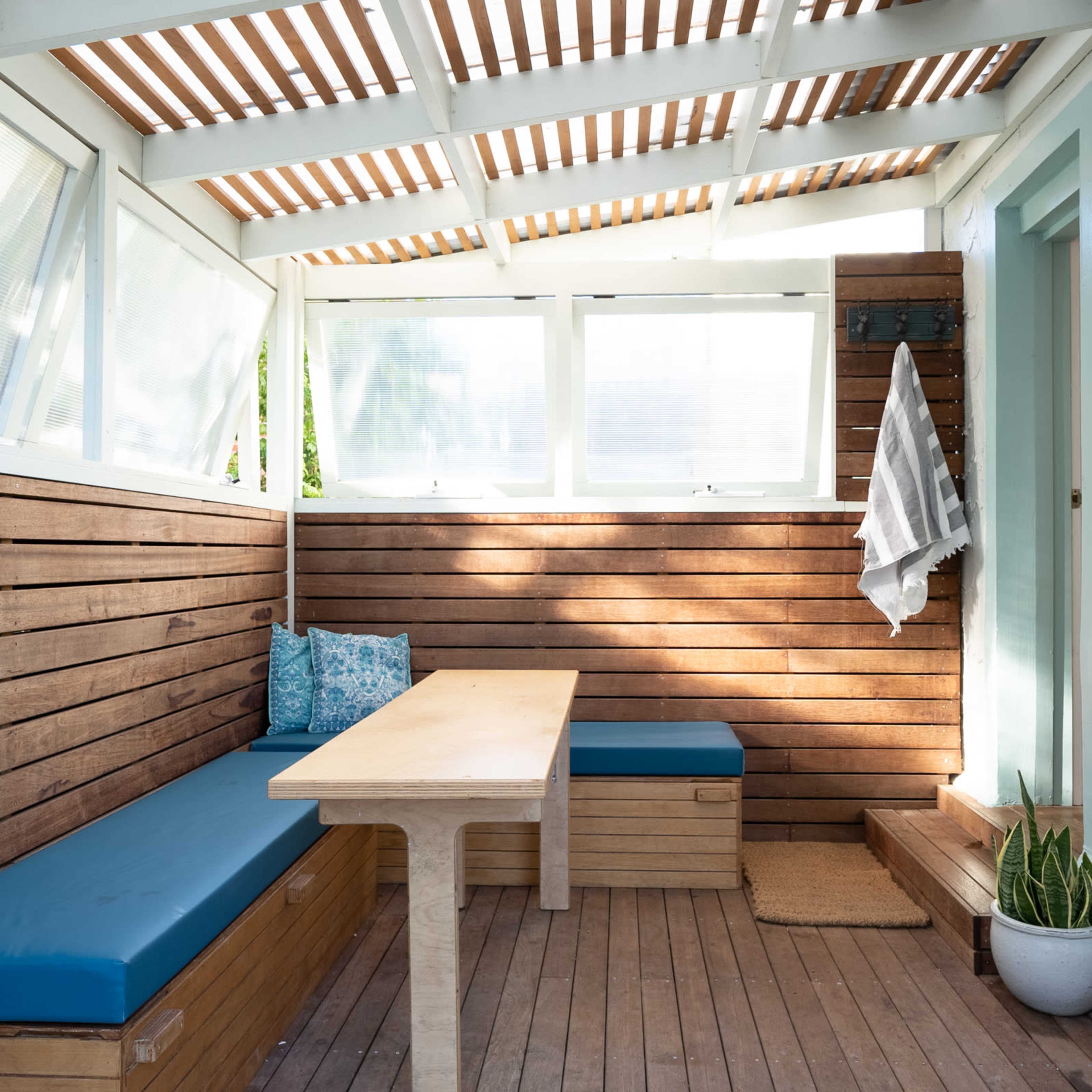 A cozy, sunlit patio with wooden walls, a table, and built-in benches.