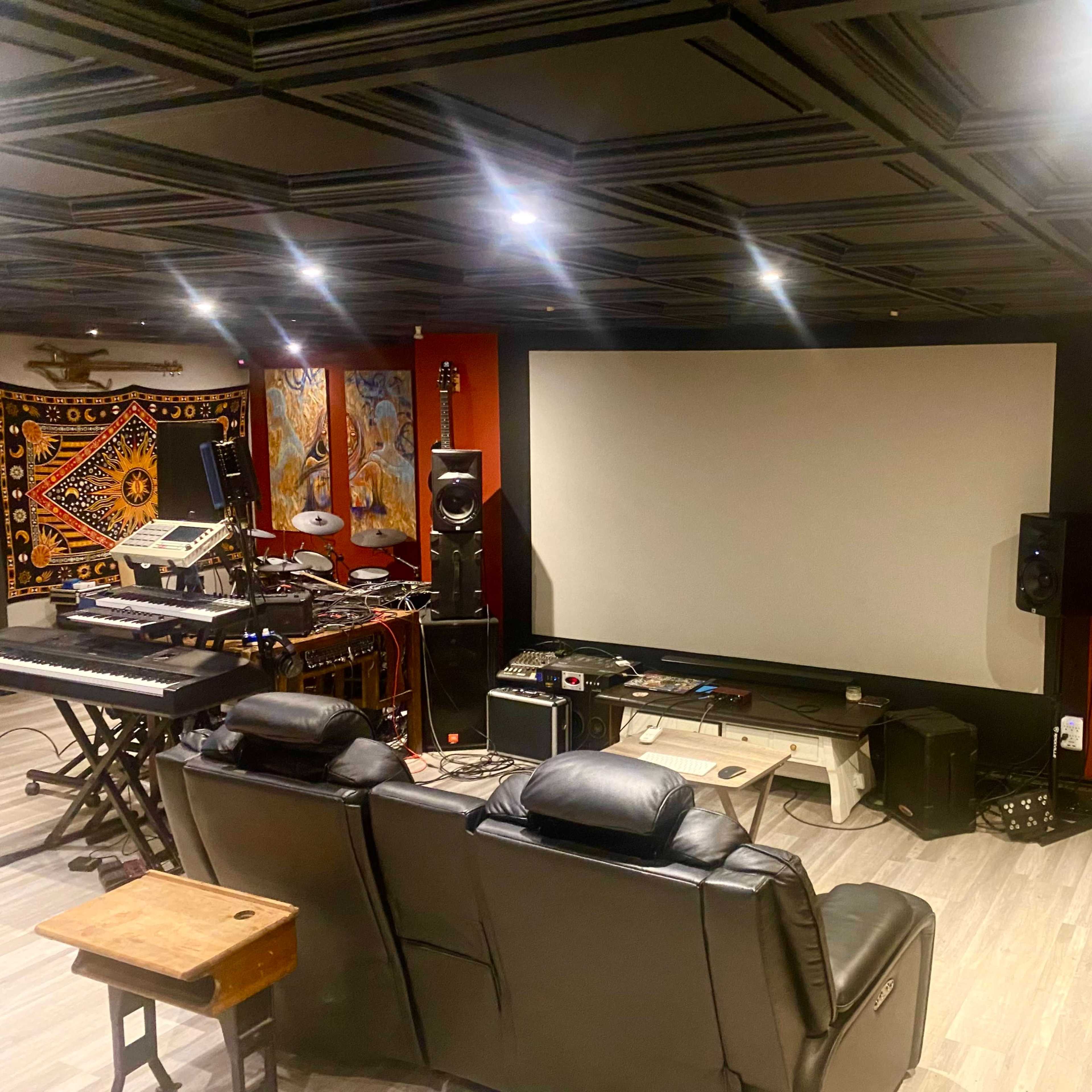 A home theater setup featuring a large blank screen, seating area with black recliners, and various audio and video equipment.