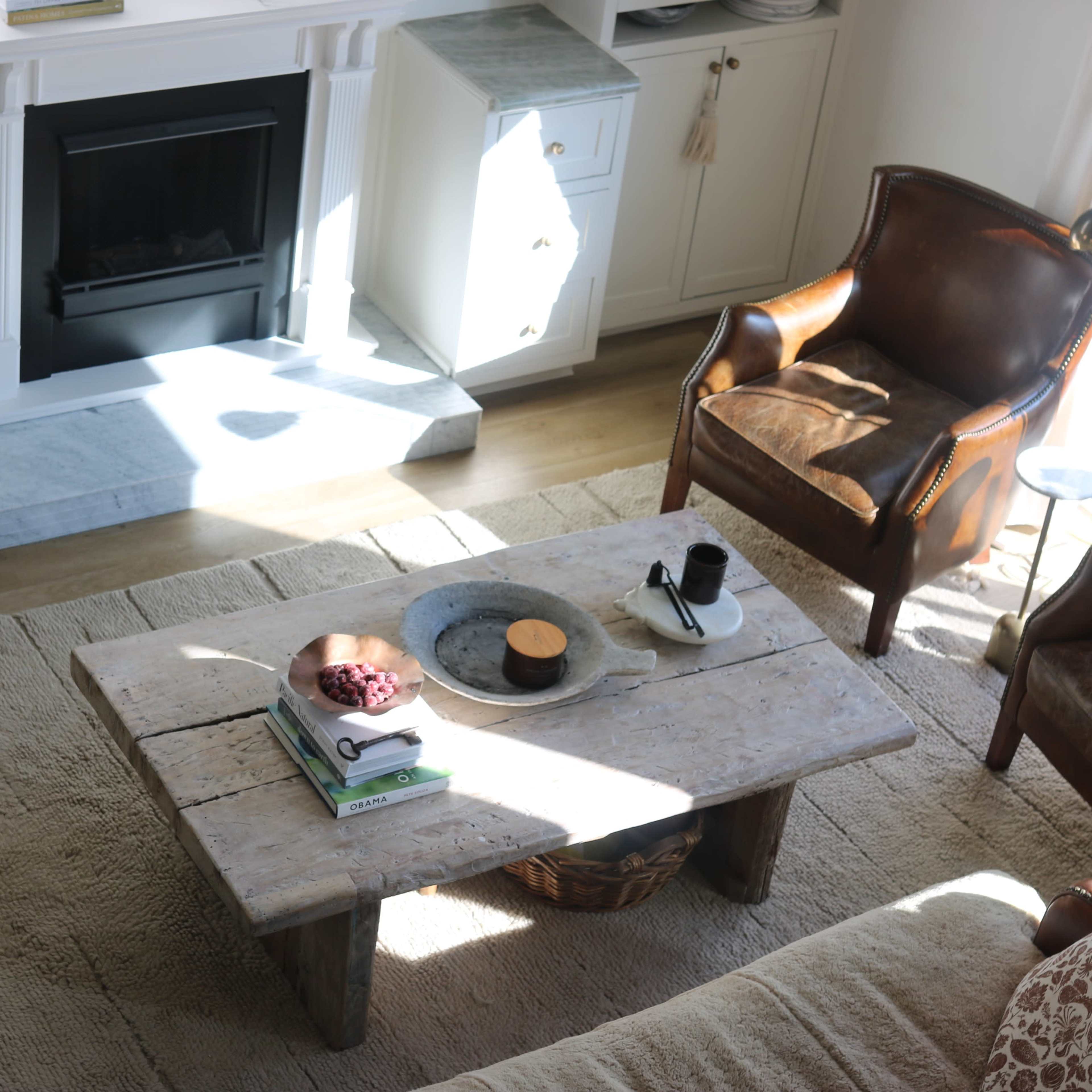 A cozy living room features a wooden coffee table with snacks and a drink, surrounded by two leather chairs and a soft area rug.