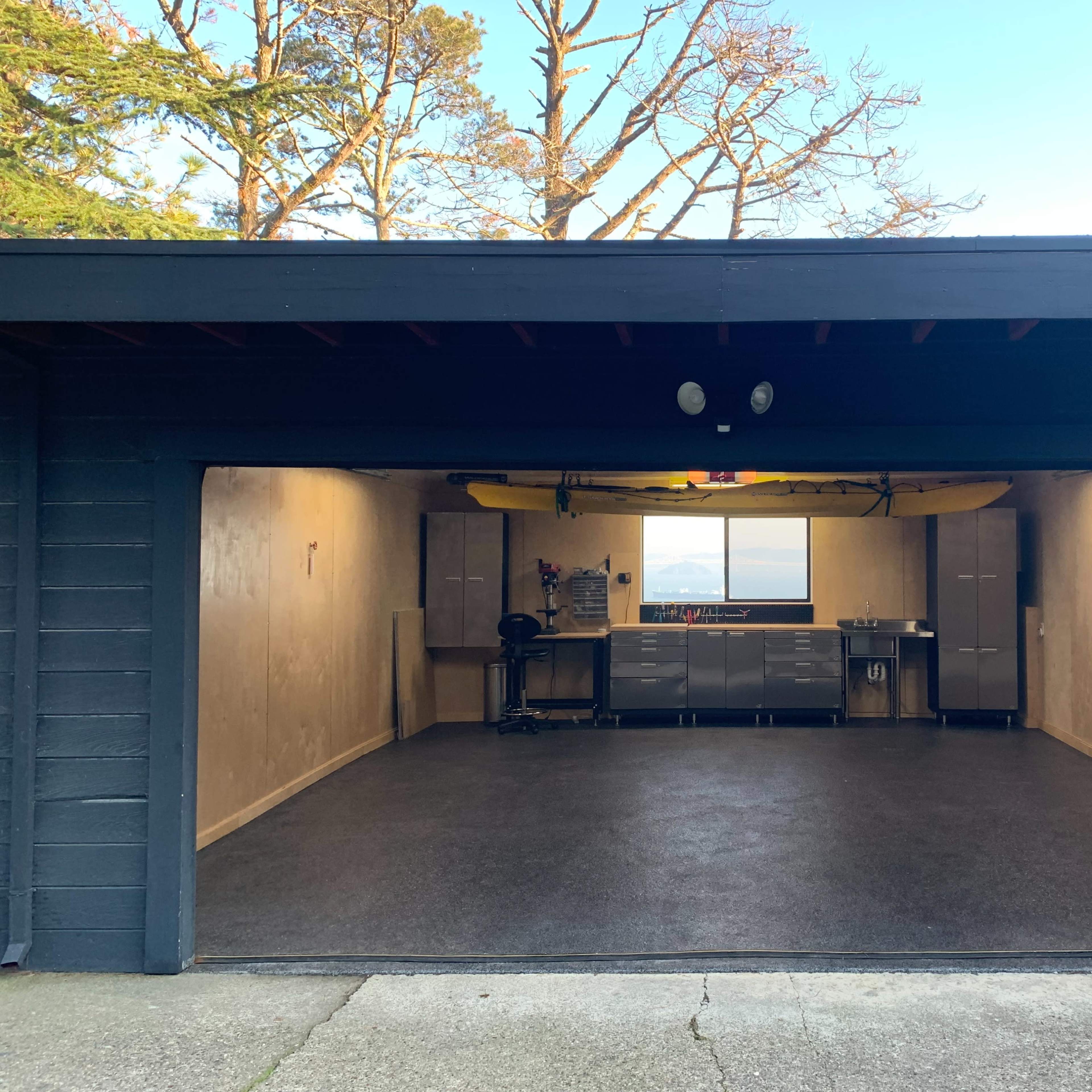 A spacious garage with a workbench and a kayak mounted on the ceiling, illuminated by natural light from a window.