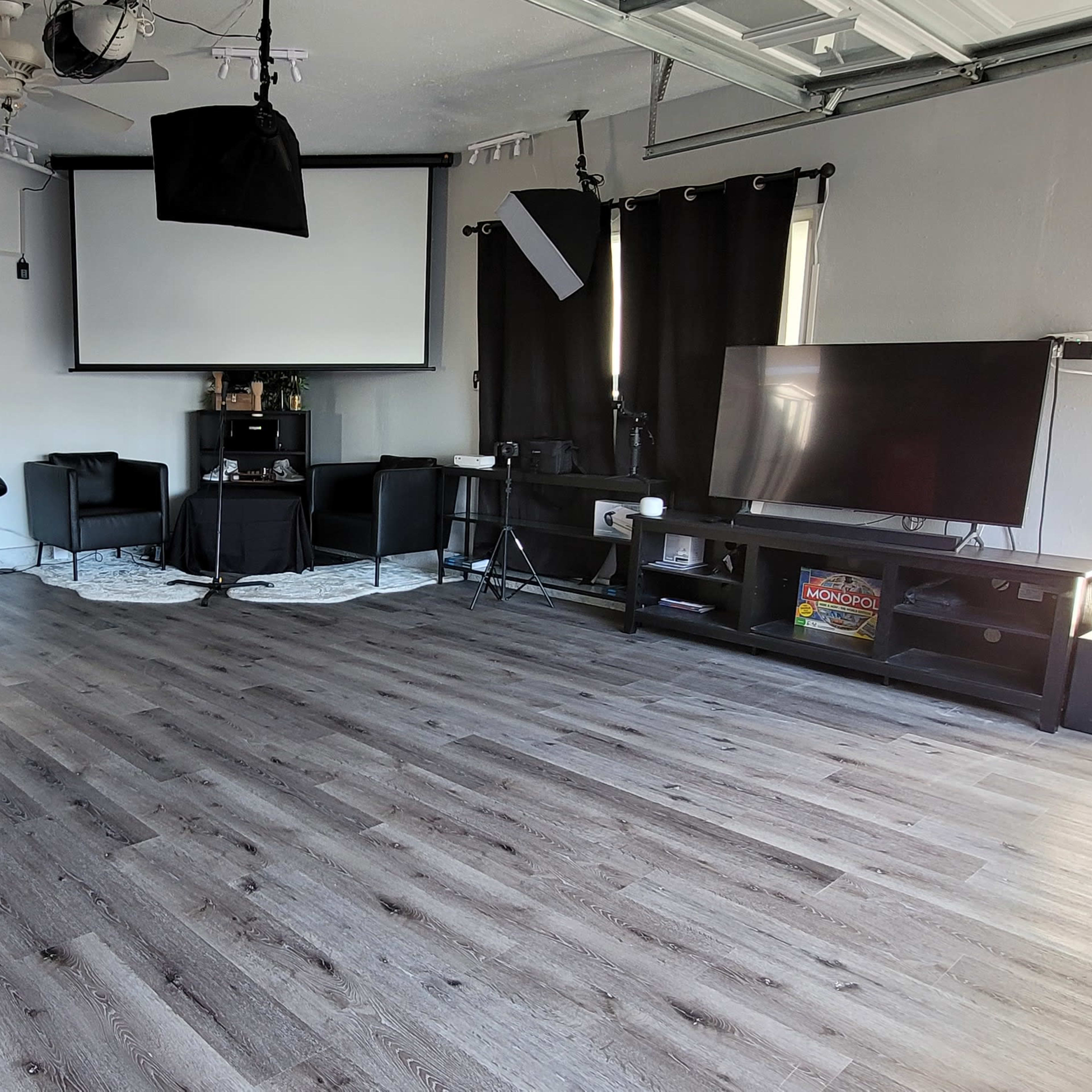 The room features a large, empty space with a smooth floor, equipped with a projection screen, a TV, several black chairs, and softbox lighting setups.