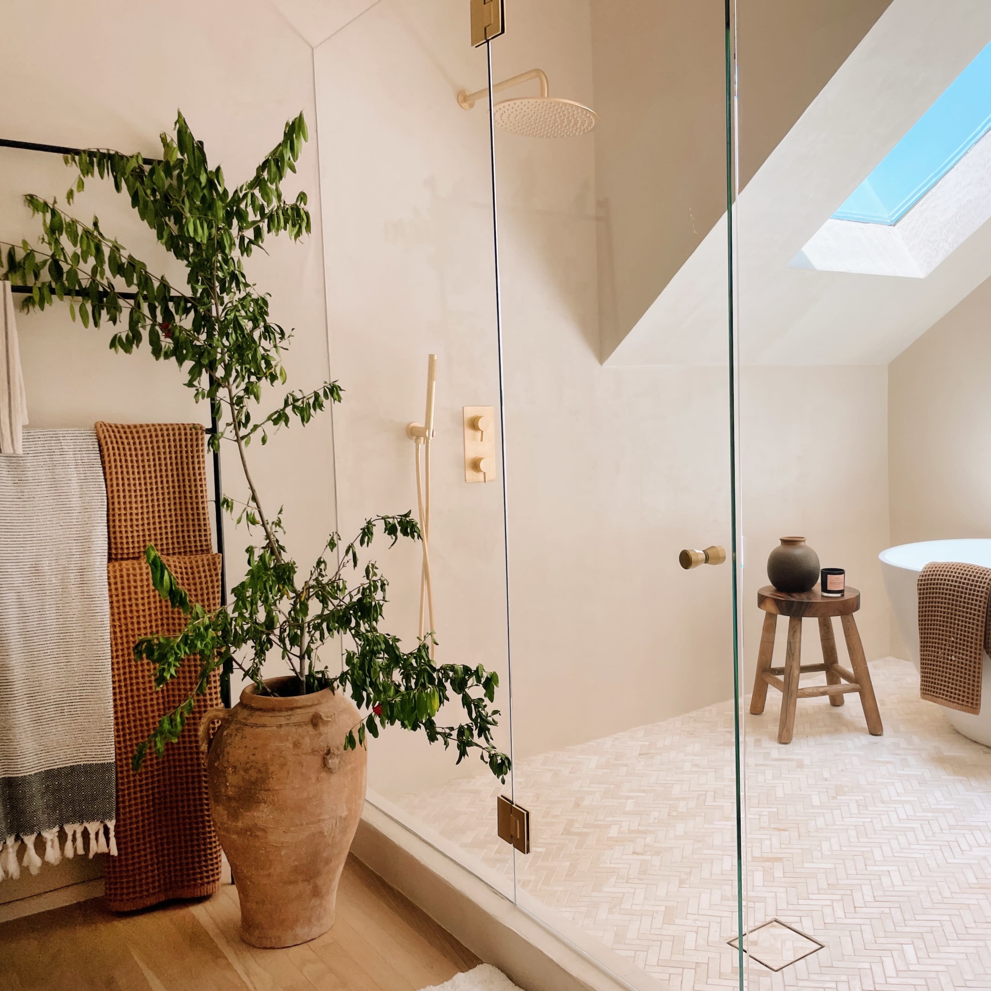 A modern bathroom featuring a glass shower enclosure, a freestanding bathtub, and a potted plant beside a wooden stool.