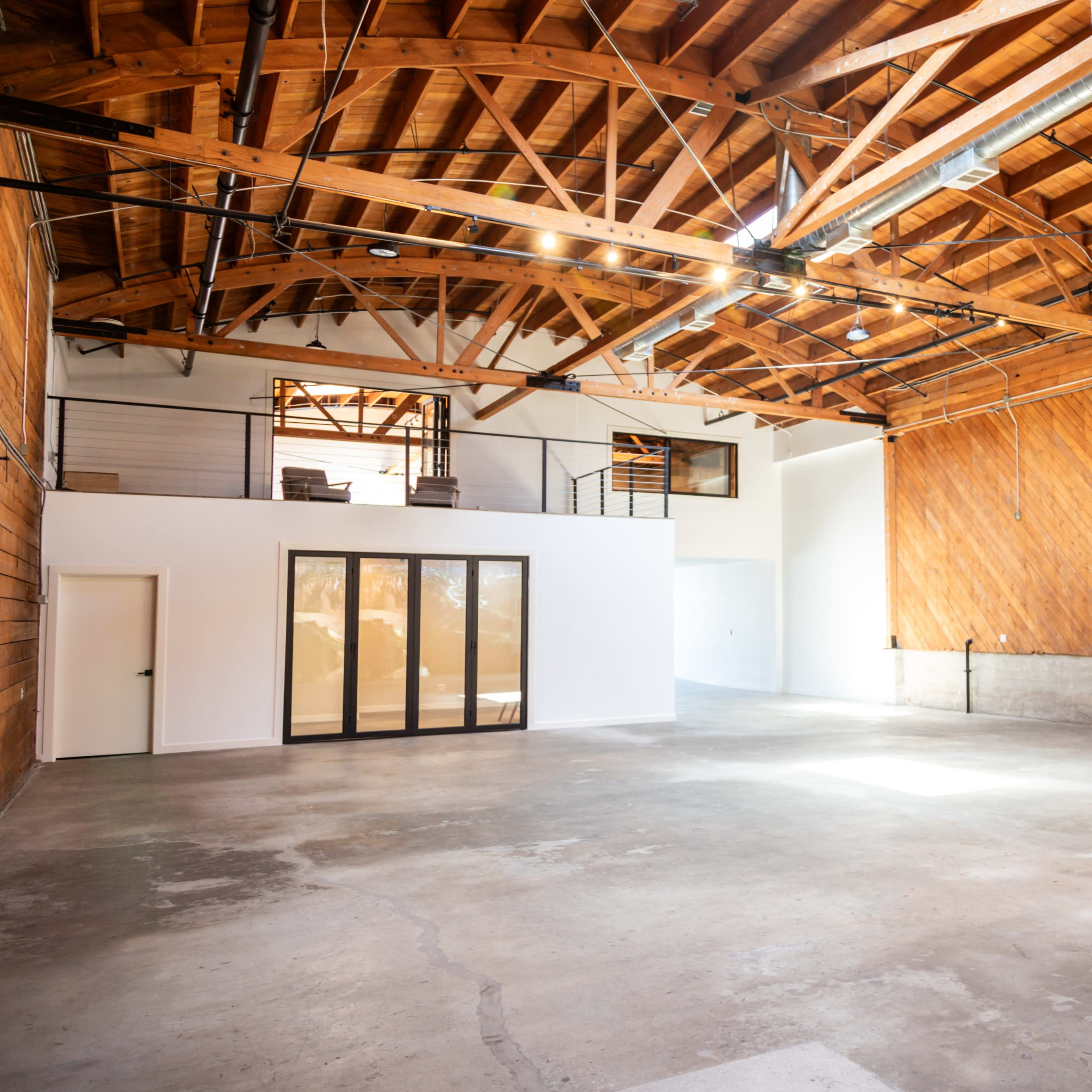 A spacious, empty industrial-style room with wooden beams and a concrete floor.