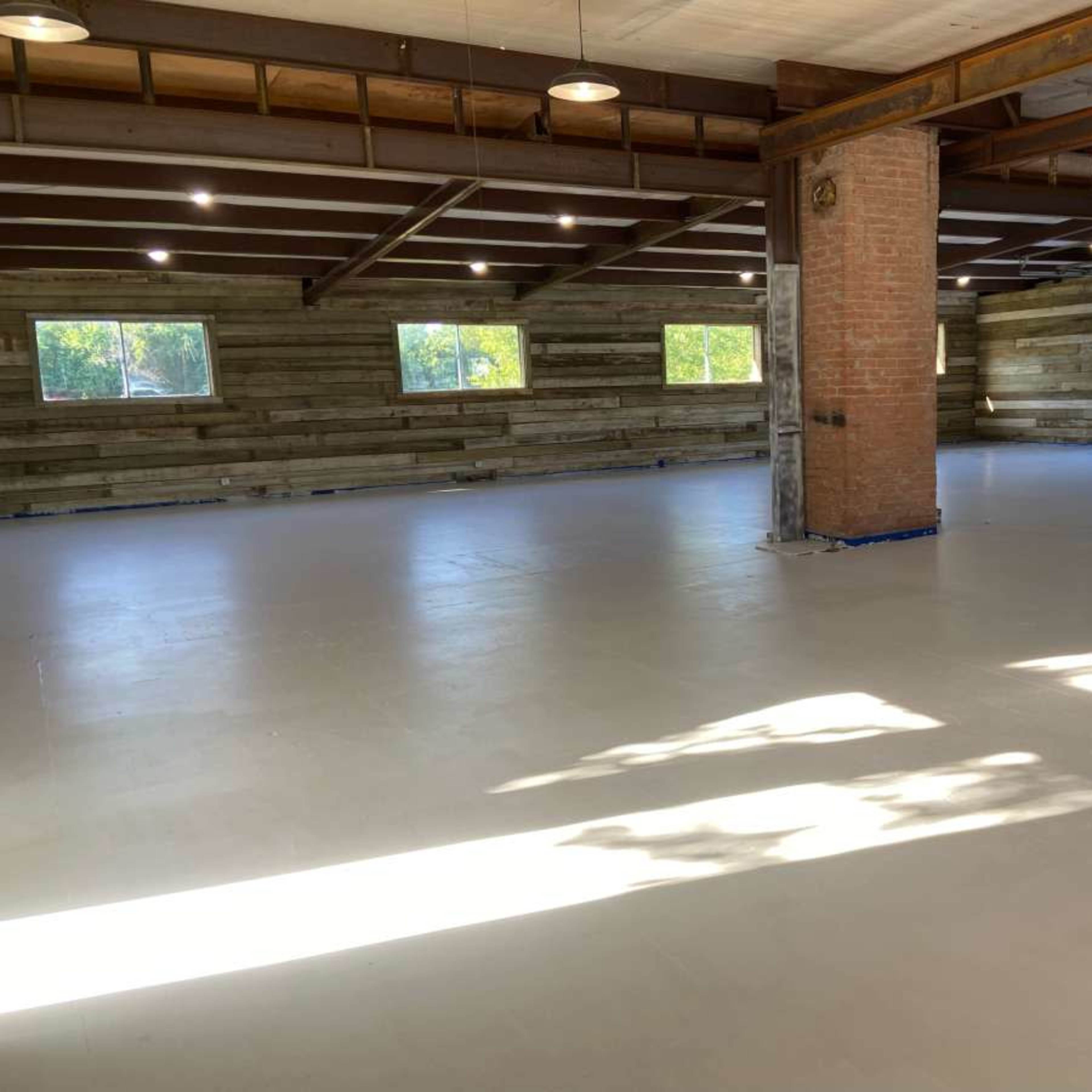 An empty industrial space with a polished concrete floor, large windows, and wooden walls.