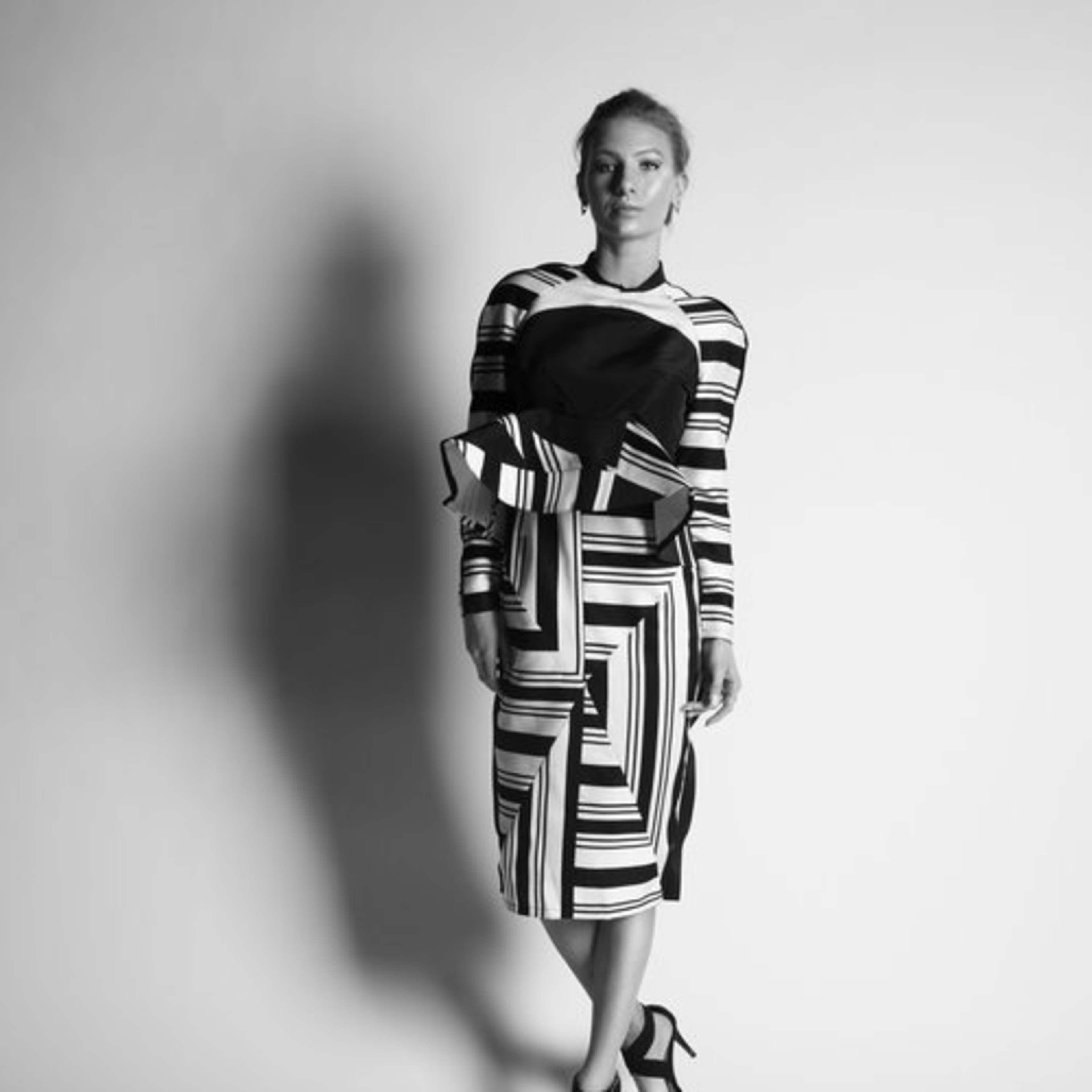 A woman poses against a plain backdrop, wearing a vertically striped outfit with a black accent.