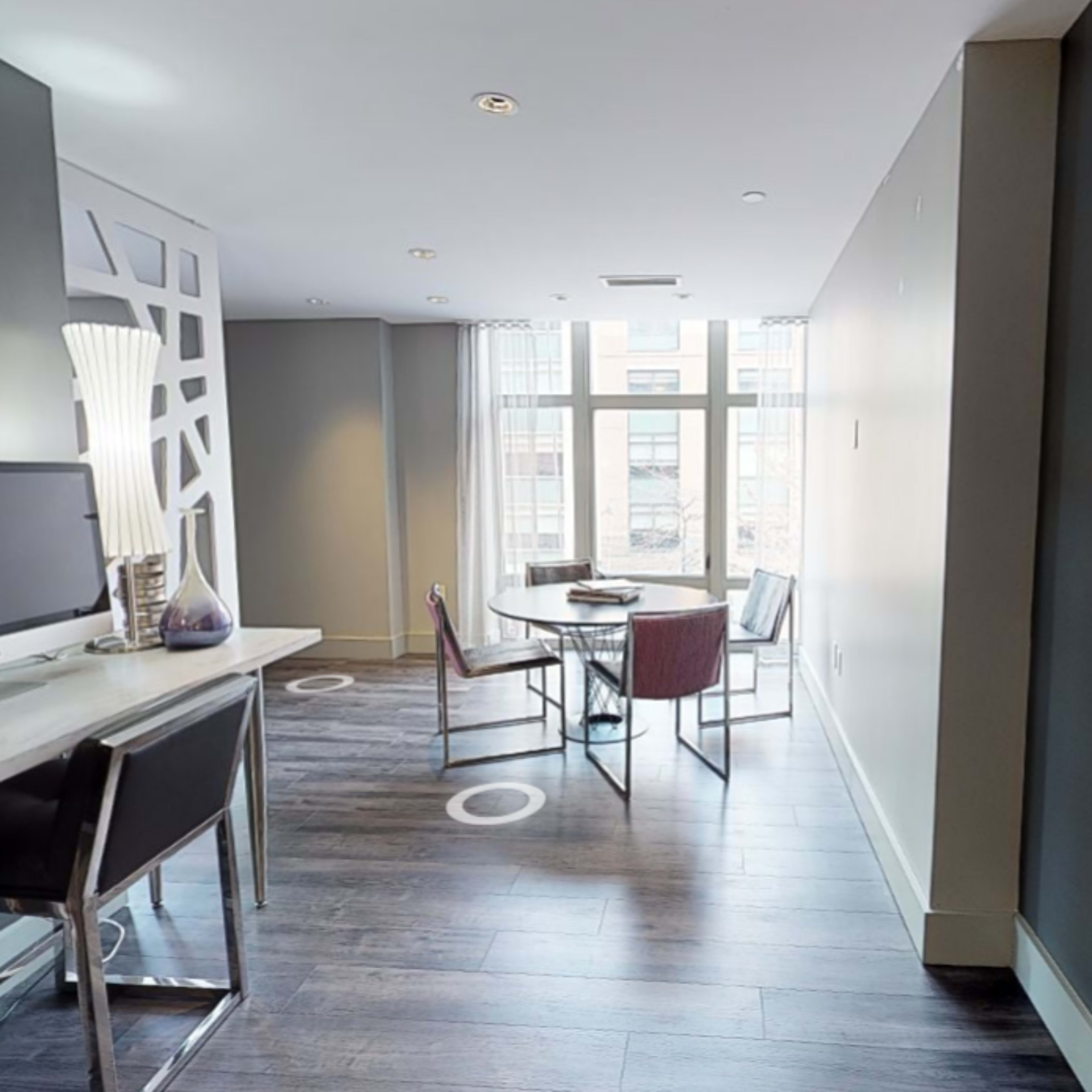 A modern dining area with a table and chairs, a computer desk, large windows, and decorative wall features.