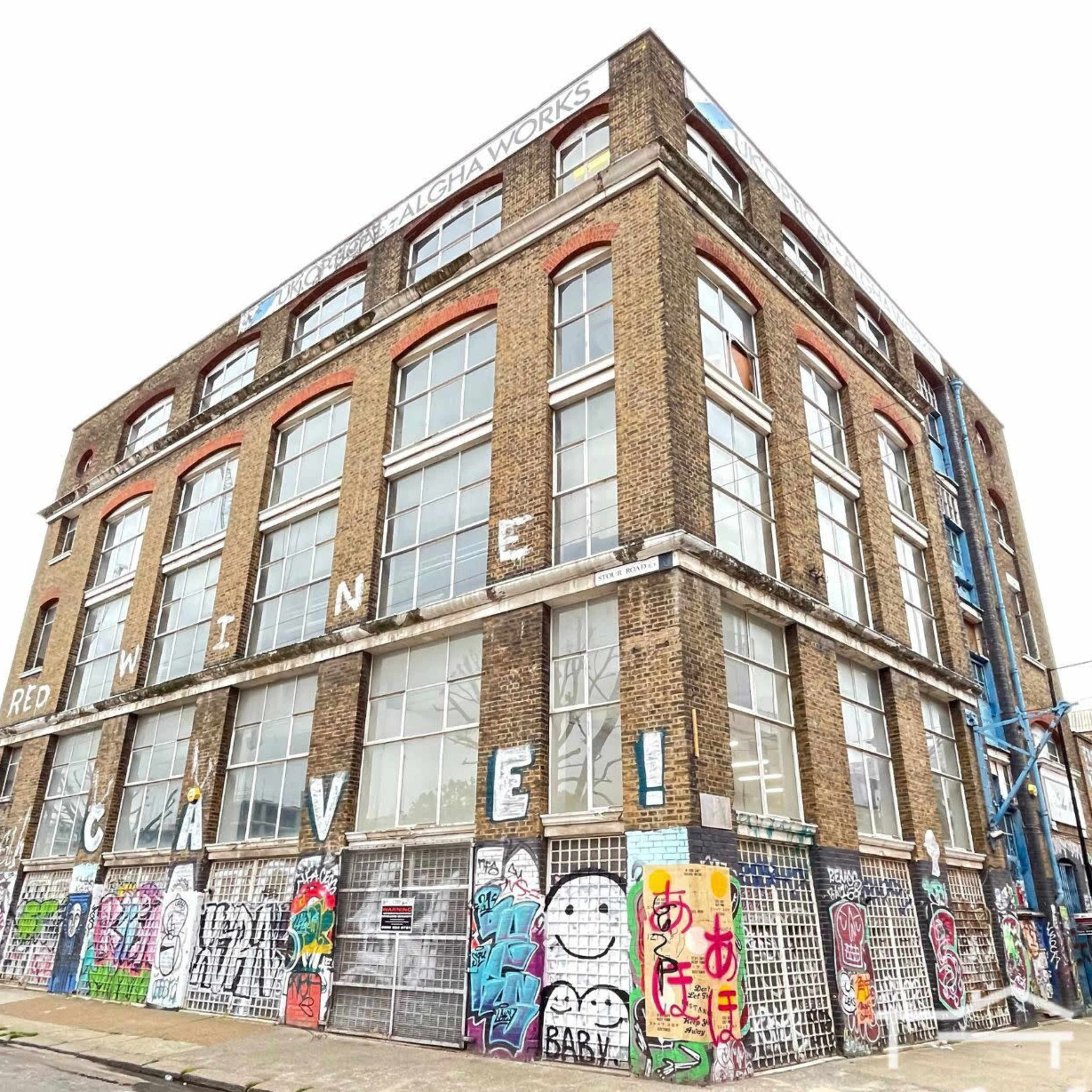 A large, brick building with multiple floors is covered in colorful graffiti and features several windows and metal grates.