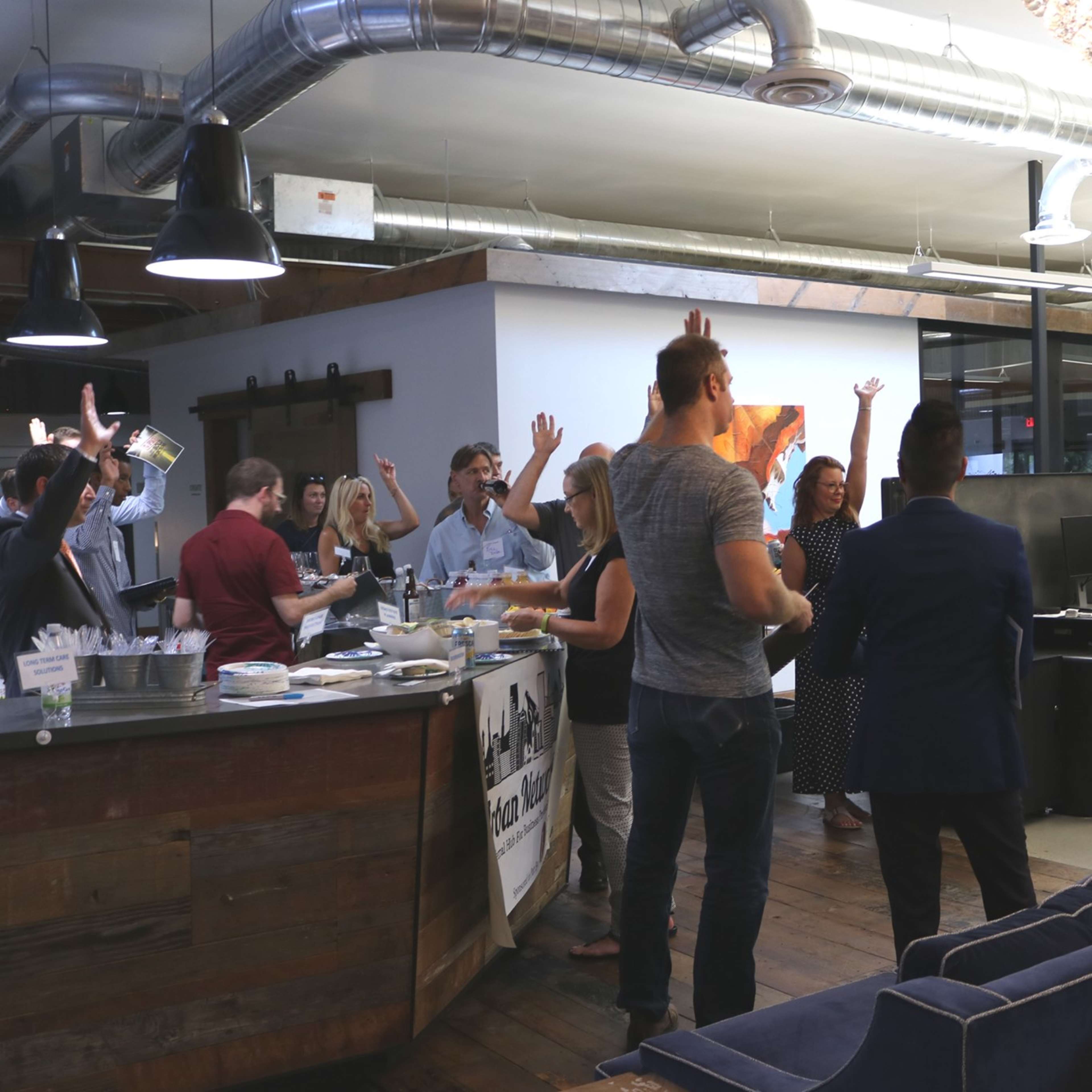 A group of people stands in a modern office space, some with hands raised, while a speaker addresses them.