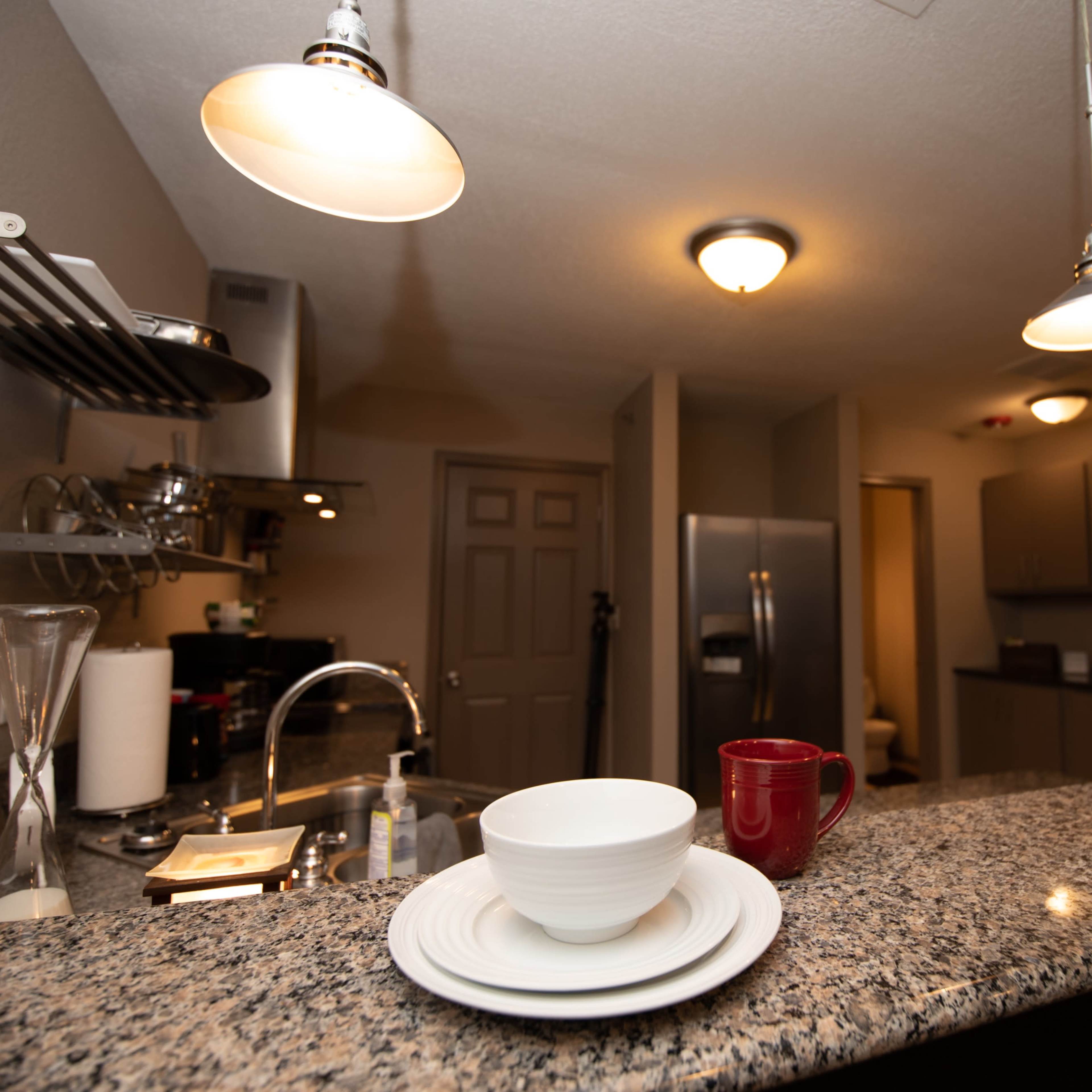 A modern kitchen with granite countertops, two empty bowls on white plates, a red mug, and stainless steel appliances.
