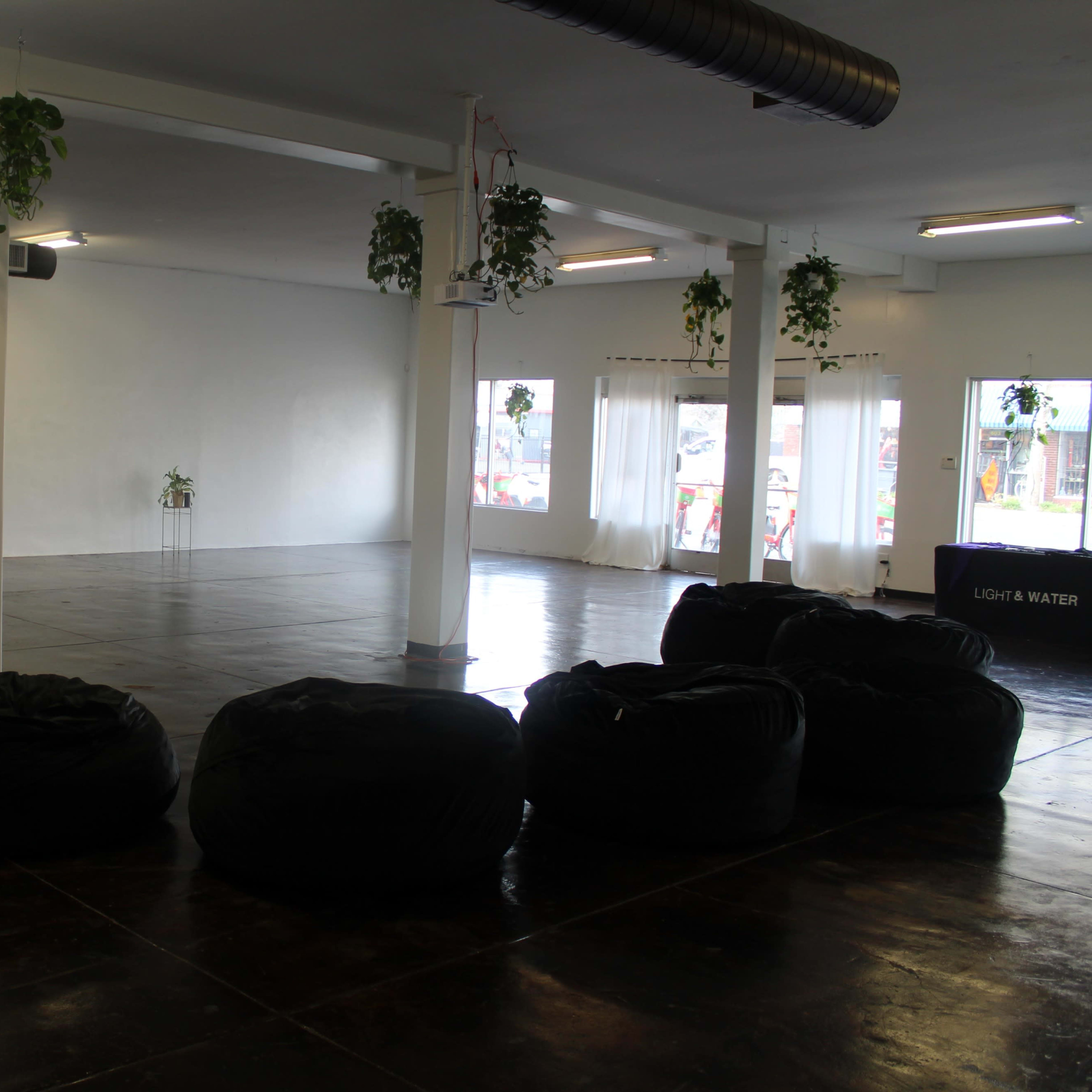 A spacious, empty room with a polished floor, a few hanging plants, and several black bean bag chairs arranged in the foreground.